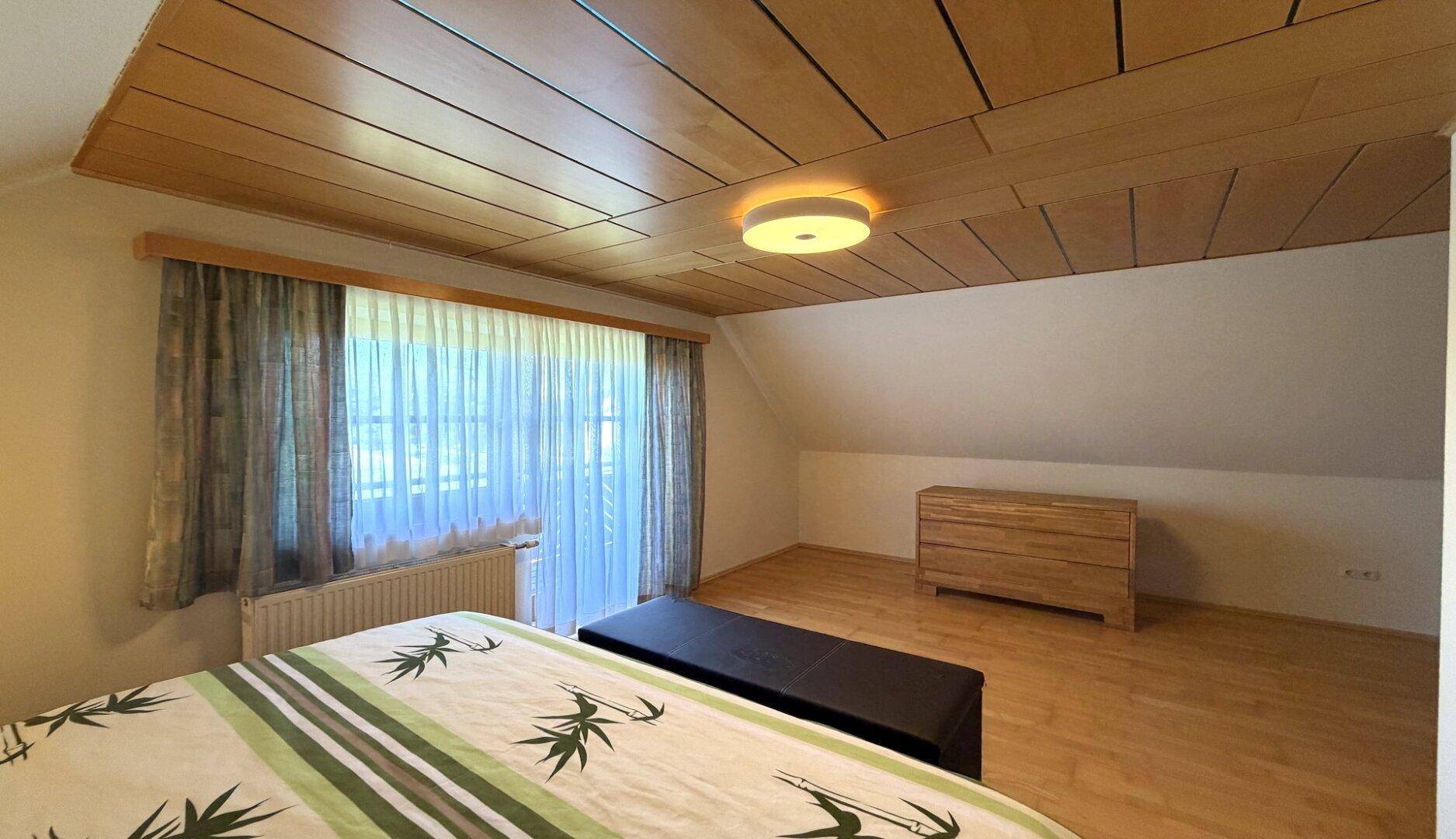 Helles Schlafzimmer mit Holzboden, Holzbalkendecke und Blick ins Grüne.