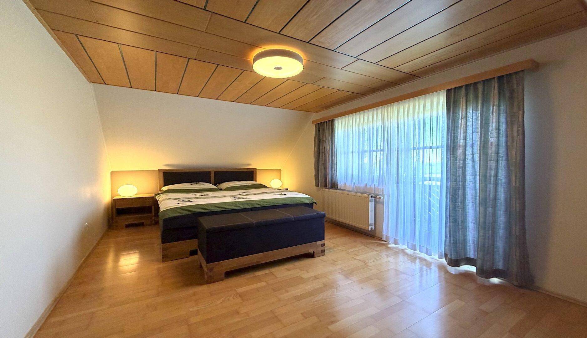 Schlafzimmer mit Holzbalkendecke, Doppelbett und Zugang zum Balkon.