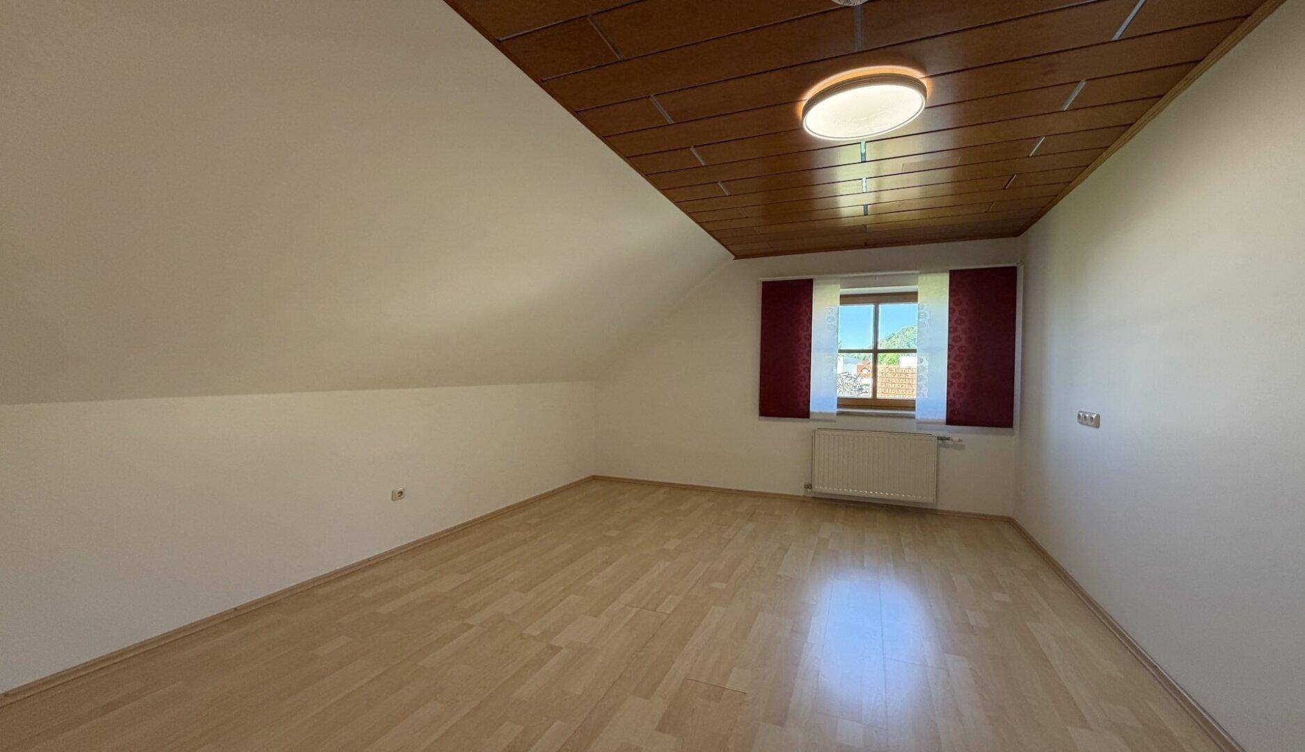 Ruhiges Schlafzimmer mit Holzboden, Dachschräge und Fenster.