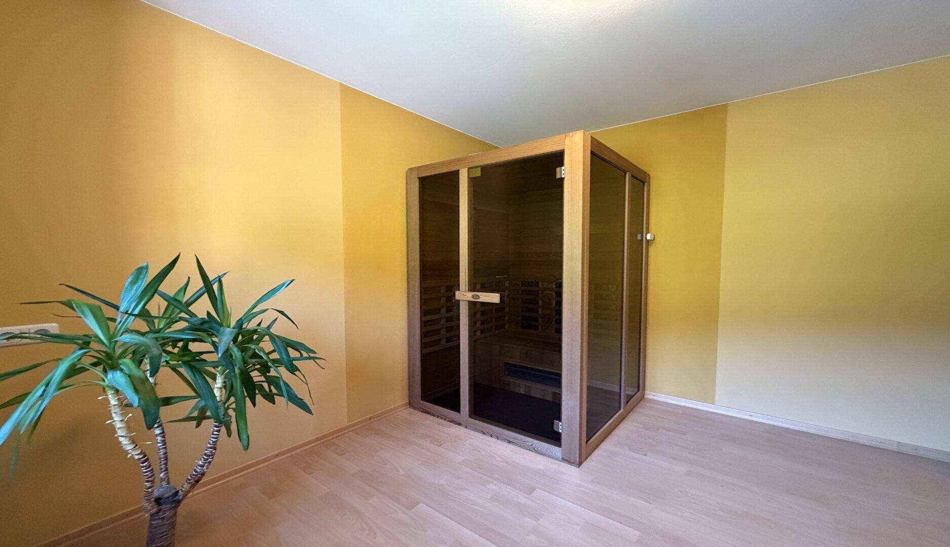 Moderne Sauna-Kabine in einem hellen Raum mit gelben Wänden und Holzfußboden.