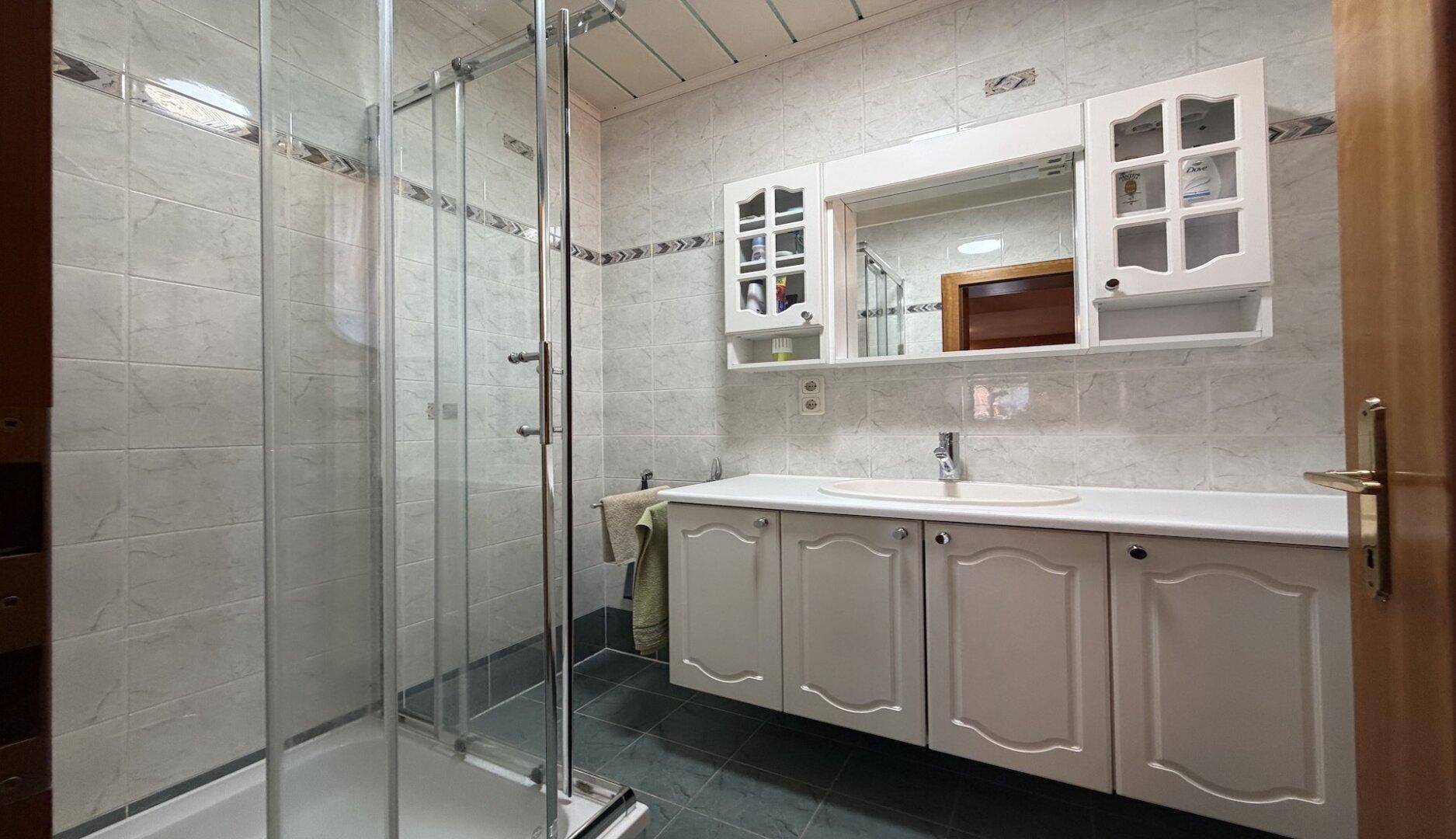 Helles Badezimmer mit Duschkabine, Waschtisch und Spiegelschrank in klassischem Stil.