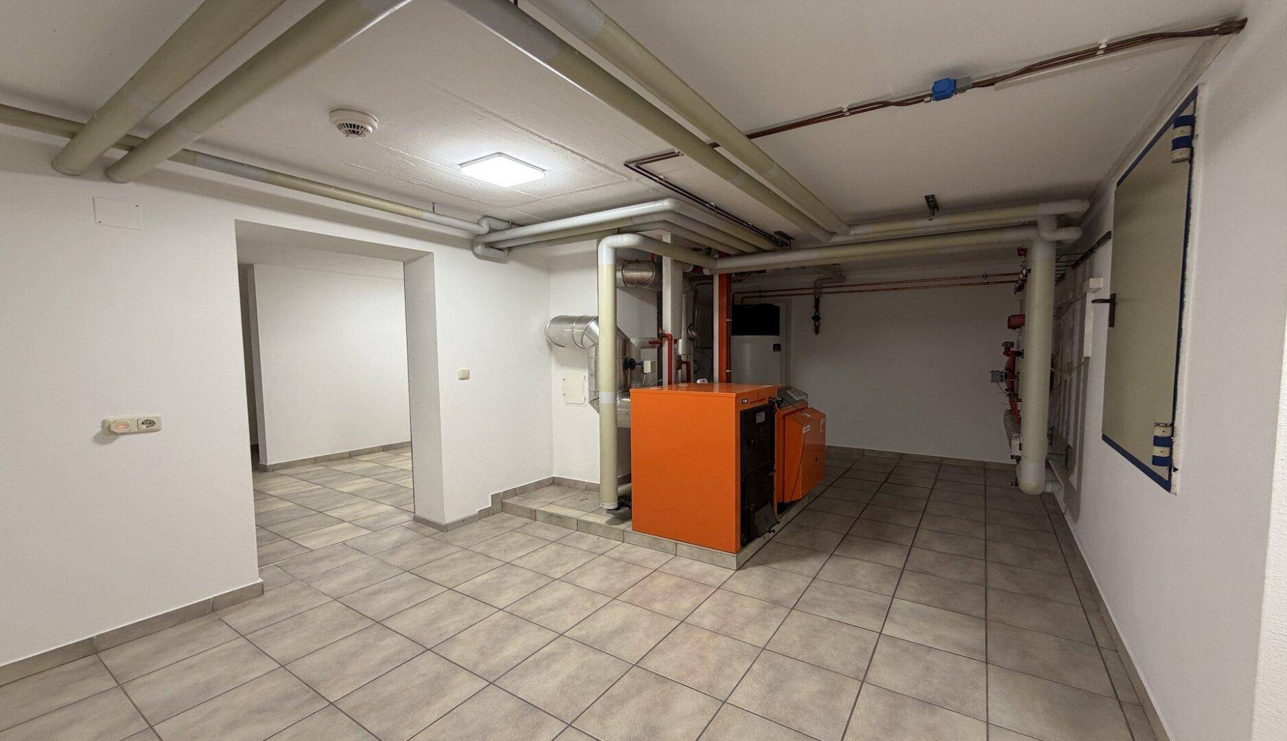 Heizungsraum im Keller mit orangefarbener Heizungsanlage und sichtbaren Rohren.