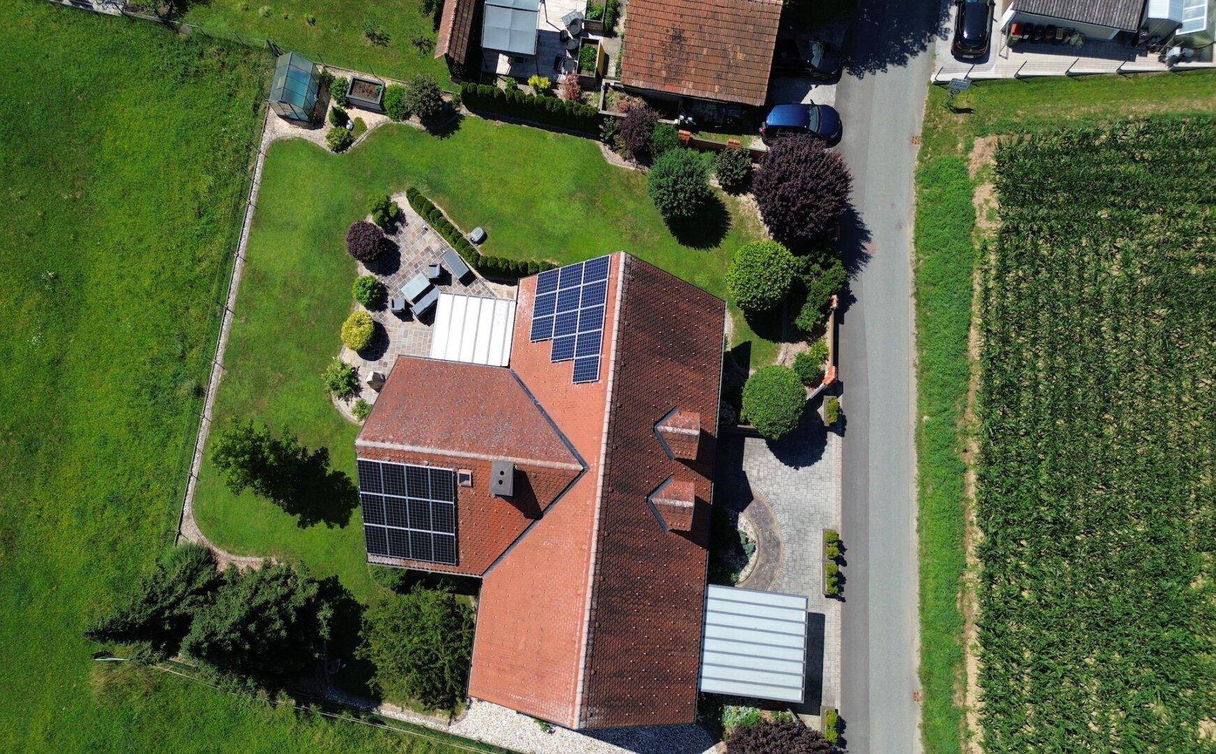 Luftaufnahme eines Hauses mit Photovoltaikanlage auf dem Dach und großem Garten.