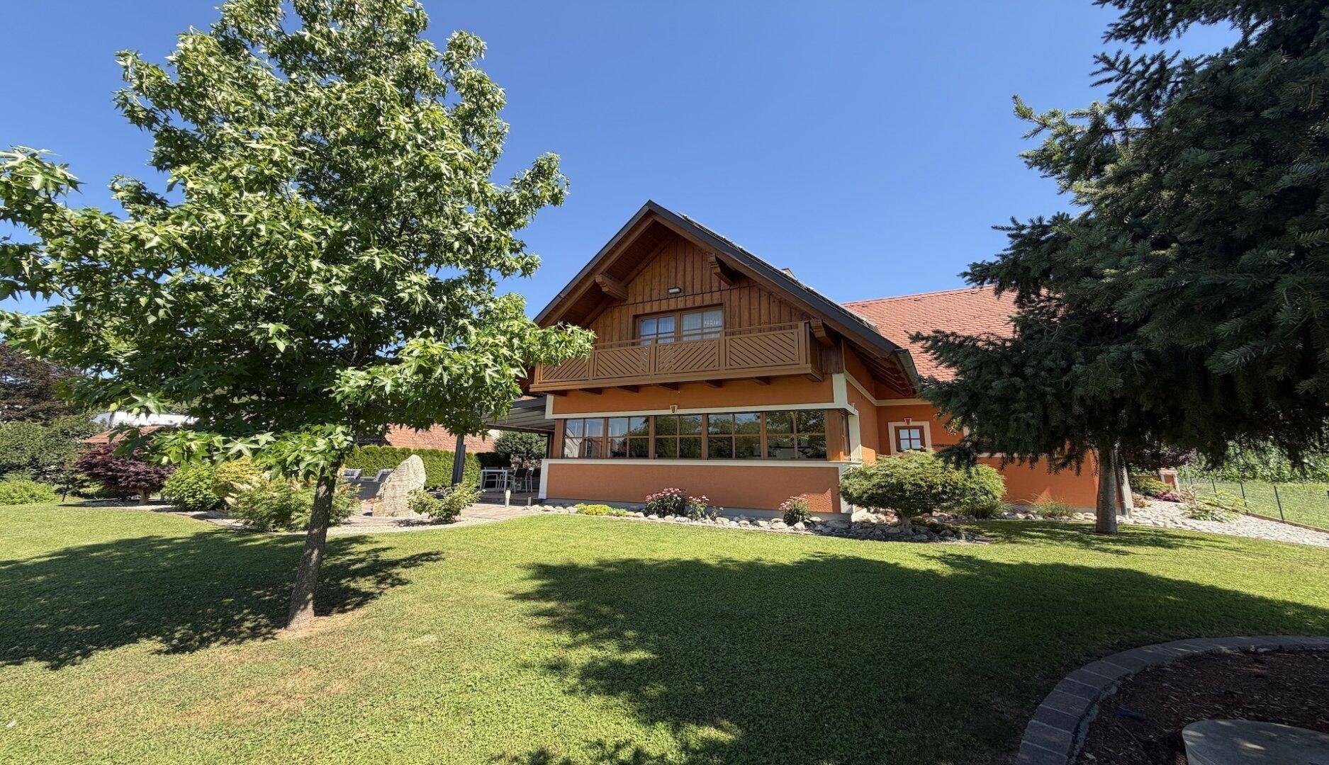 Gepflegtes Haus mit Balkon, weitläufigem Garten und altem Baumbestand.