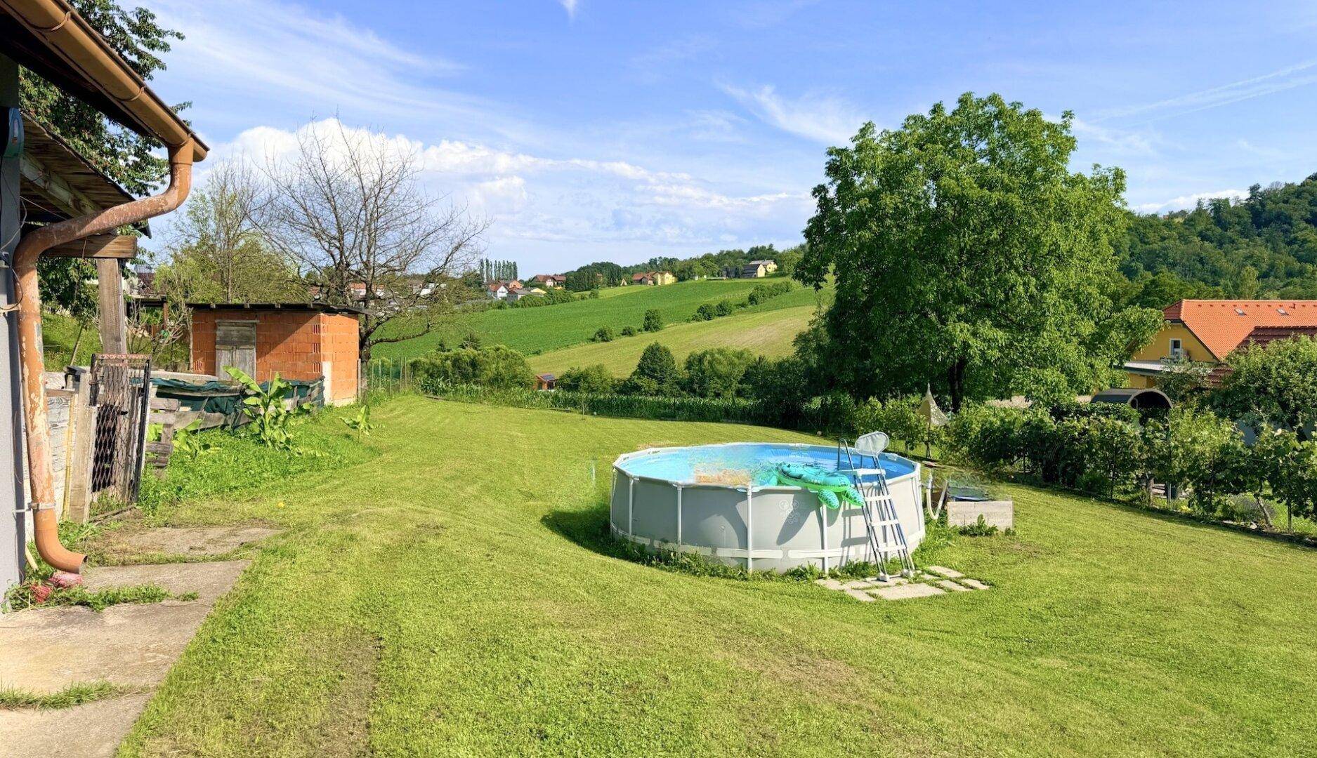 Grüner Garten mit einem Aufstellpool und weitem Blick über die hügelige Landschaft.