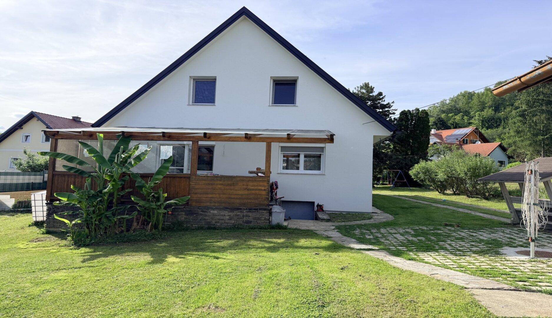 Seitenansicht des Hauses mit überdachter Terrasse und gepflegtem Rasenbereich im Garten.