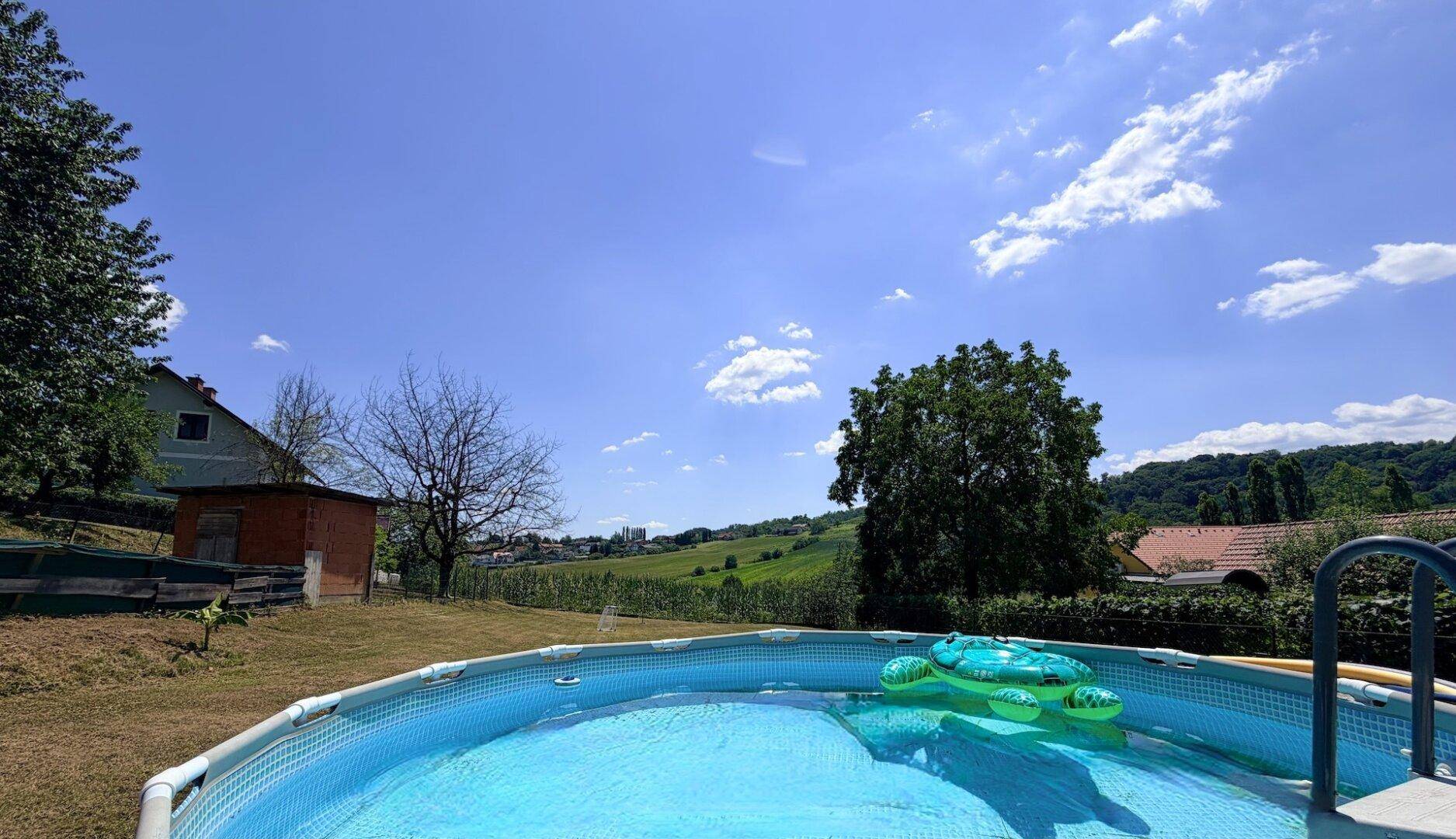 Nahaufnahme des Aufstellpools im Garten mit aufblasbaren Spielzeugen und blauem Himmel.