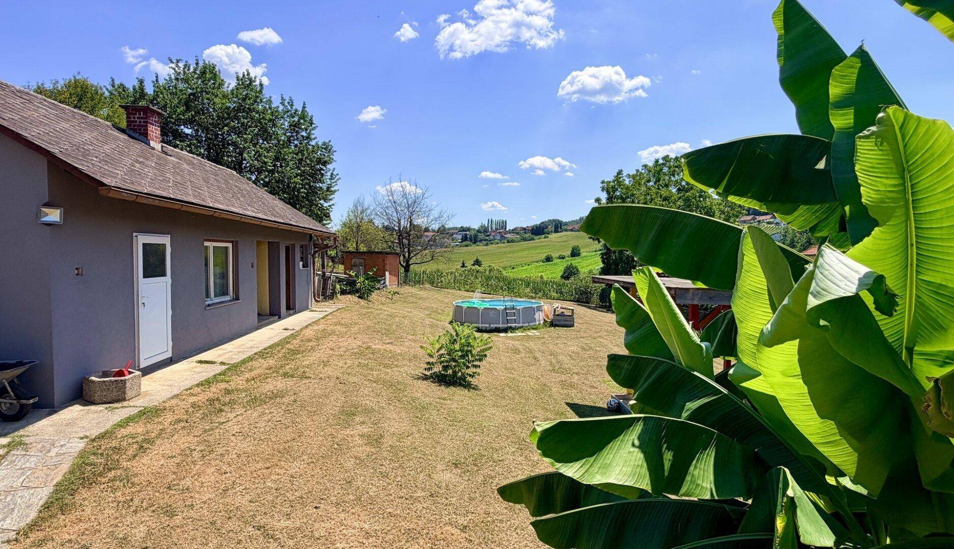 Seitenansicht des Hauses mit großem Garten, Aufstellpool und üppigen Bananenpflanzen.