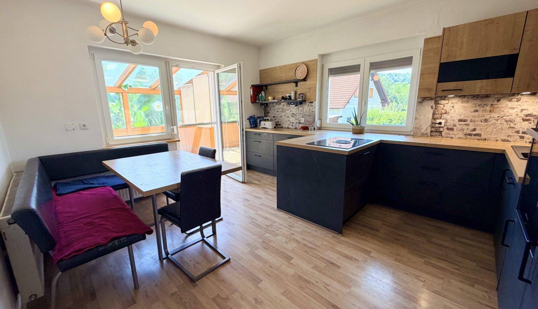 Moderne Küche mit Essbereich, Holzboden und Zugang zu einem hellen Wintergarten oder einer Terrasse.