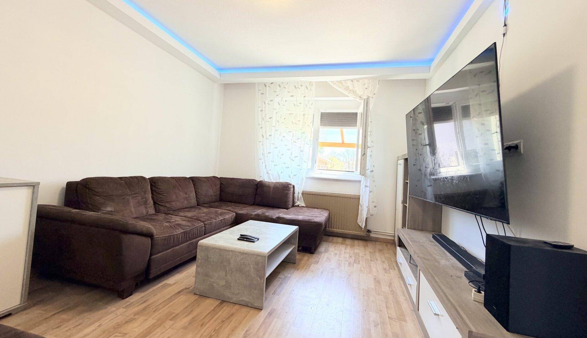 Gemütliches Wohnzimmer mit großem Ecksofa, Fernseher und indirekter Deckenbeleuchtung.
