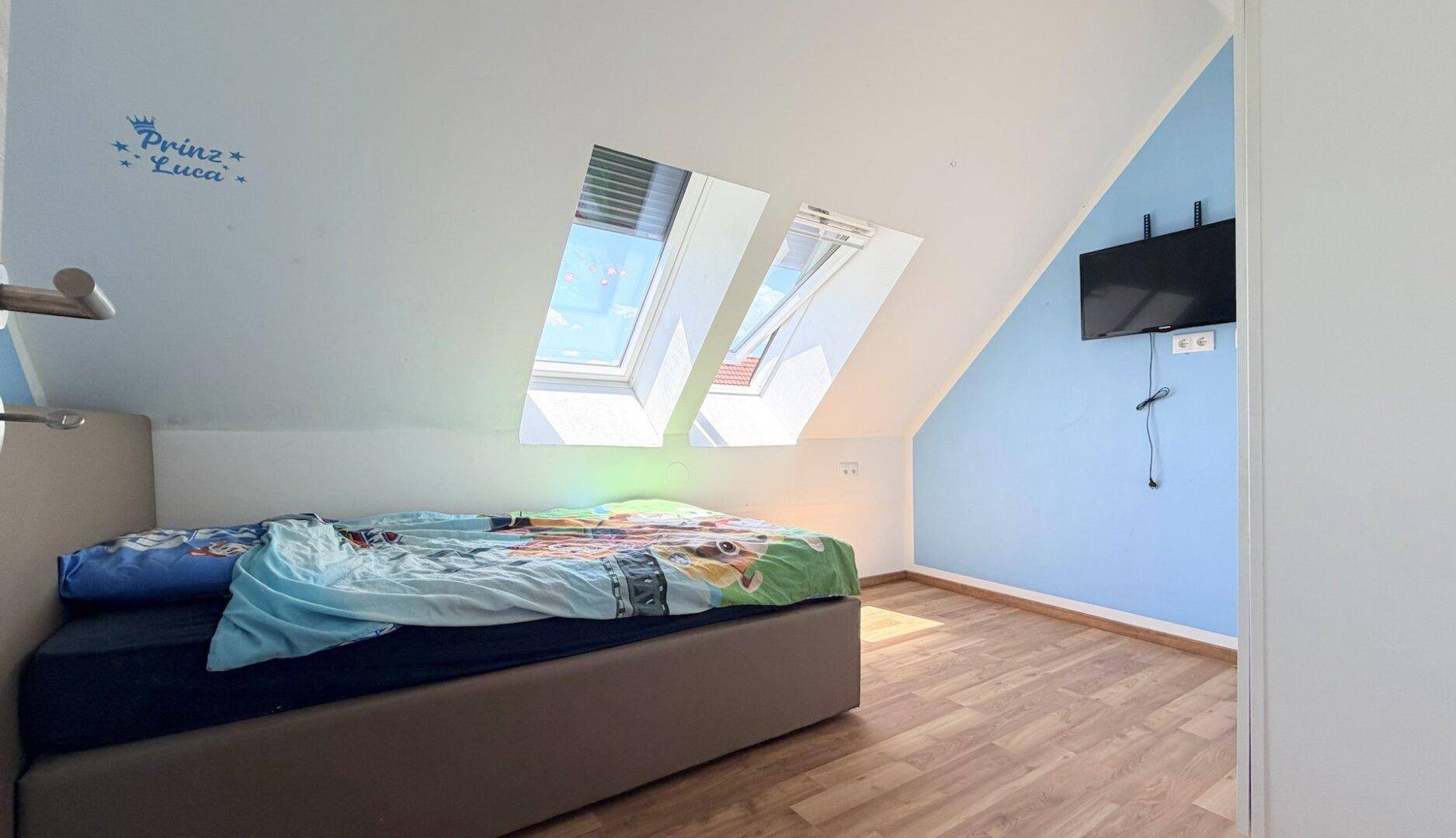 Helles Schlafzimmer im Dachgeschoss mit schräger Decke, Dachfenstern und blau gestrichenen Wänden.