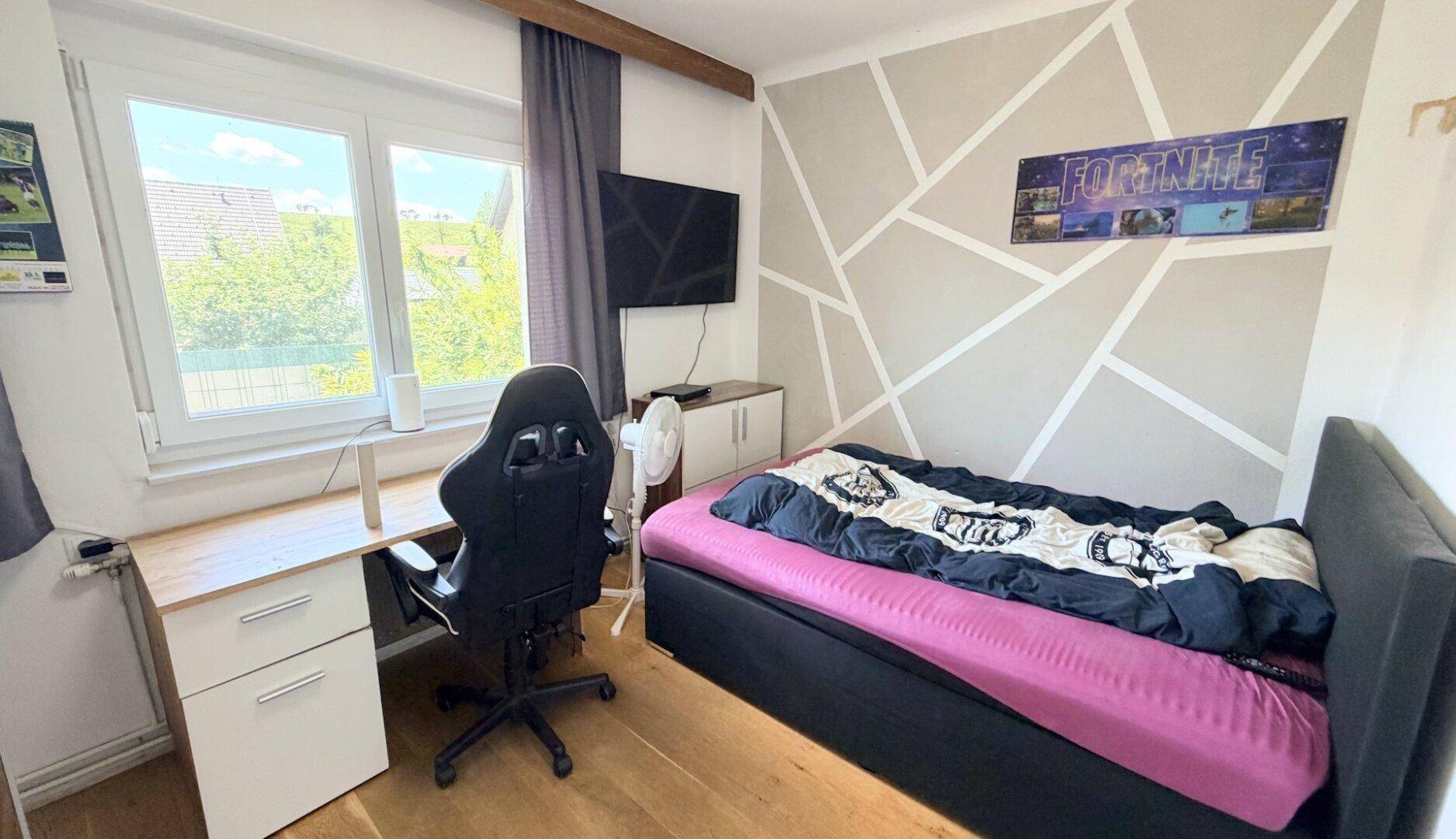 Jugendzimmer mit Bett, Schreibtisch, Gaming-Stuhl und kreativer Wandgestaltung.