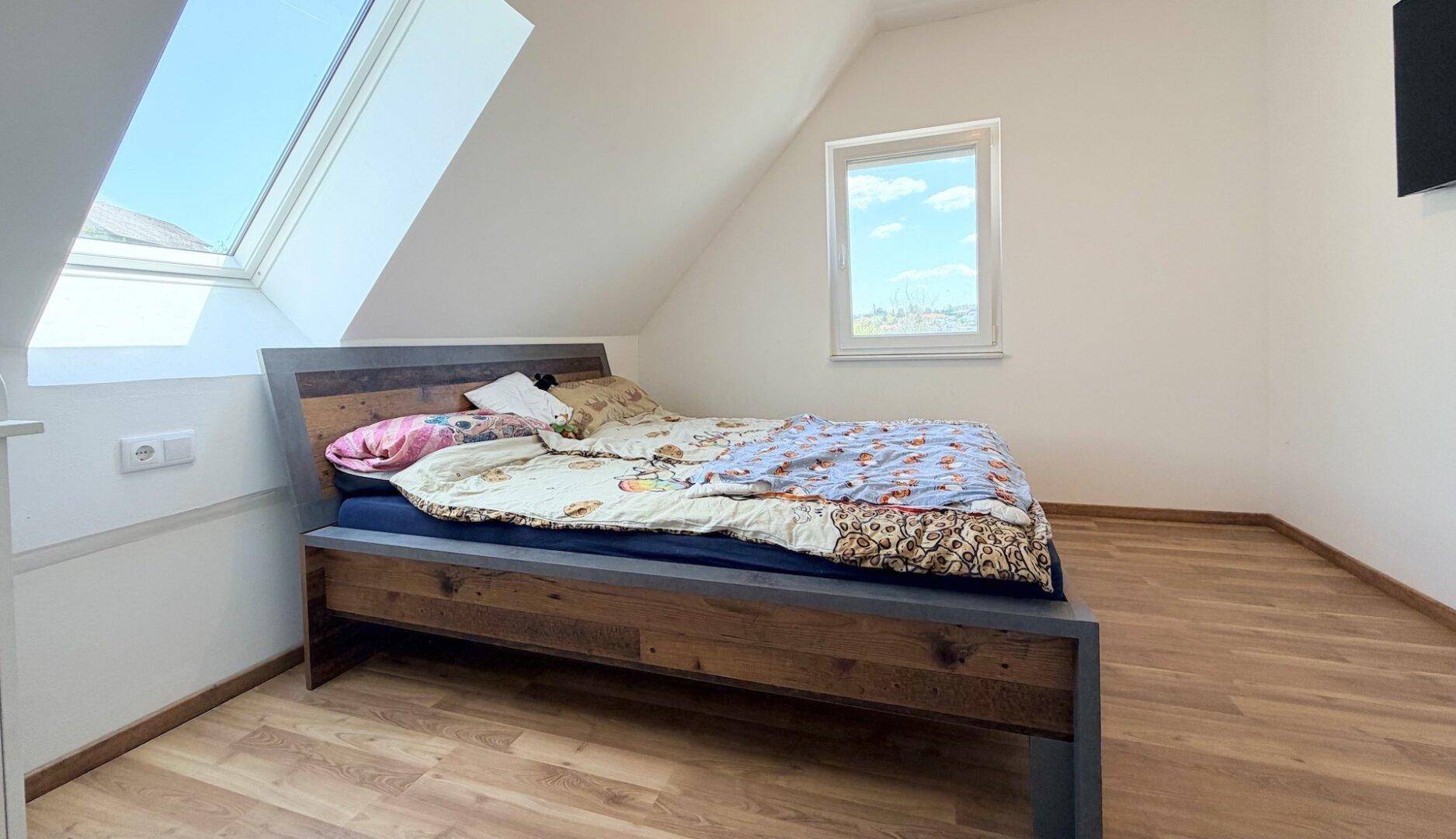 Gemütliches Schlafzimmer im Dachgeschoss mit Holzbett, Dachfenster und hellem Laminatboden.