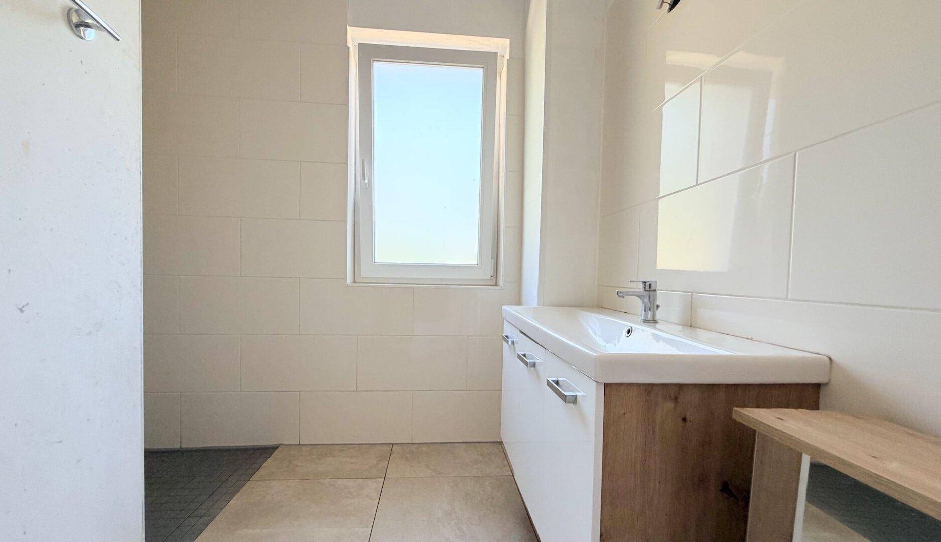 Helles Badezimmer mit weißen Wandfliesen, modernem Waschtisch und Fenster.
