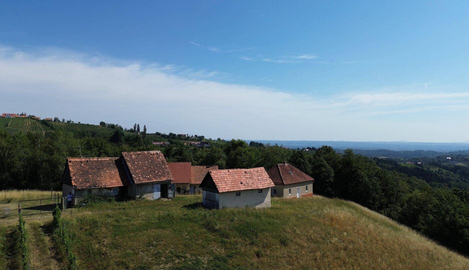 Weitläufige Ansicht mehrerer ländlicher Gebäude auf einem Hügel mit Blick auf die umliegende Landschaft und Weinberge.