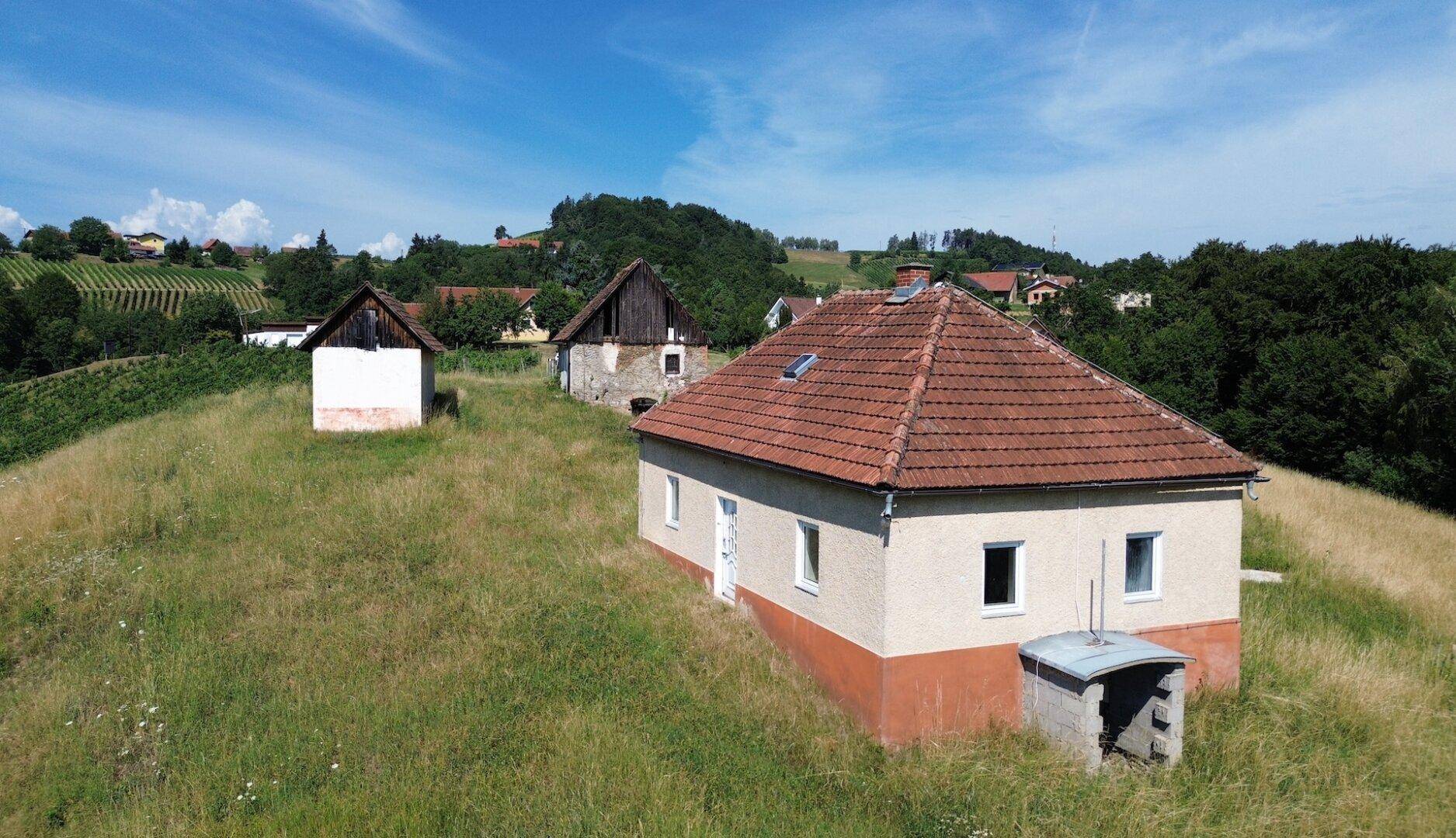 Nahaufnahme eines traditionellen Hauses mit Ziegeldach und weiteren Gebäuden im Hintergrund, eingebettet in die Natur.