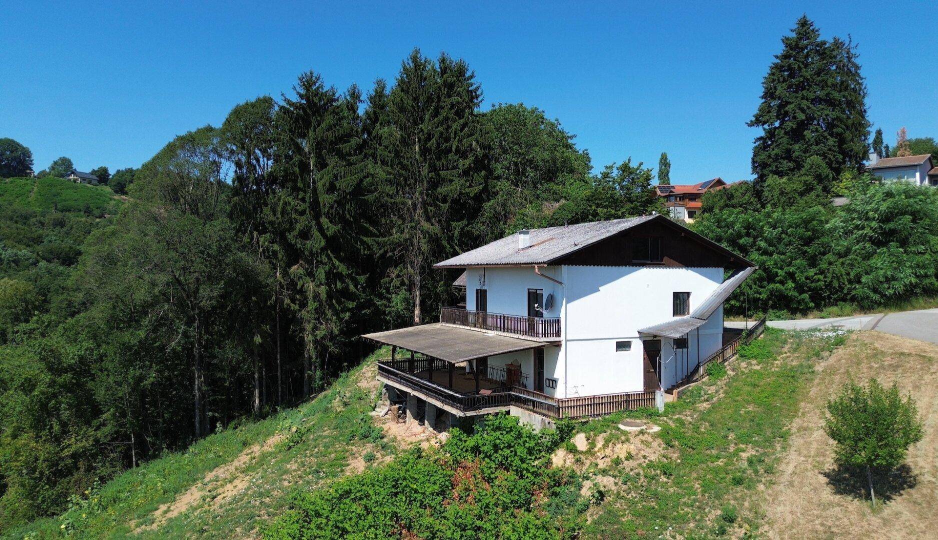 Haus in Hanglage umgeben von Bäumen und Natur, mit großem Balkonbereich.