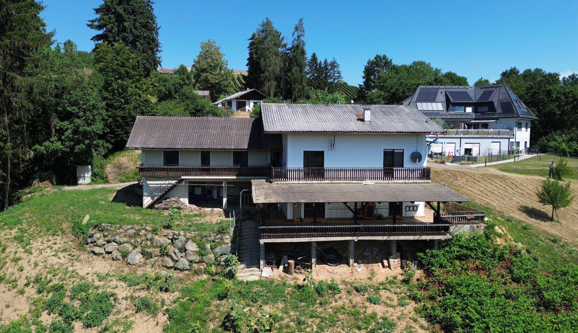 Weitläufiges Anwesen mit Haupthaus und Anbau, eingebettet in eine grüne Hügellandschaft.