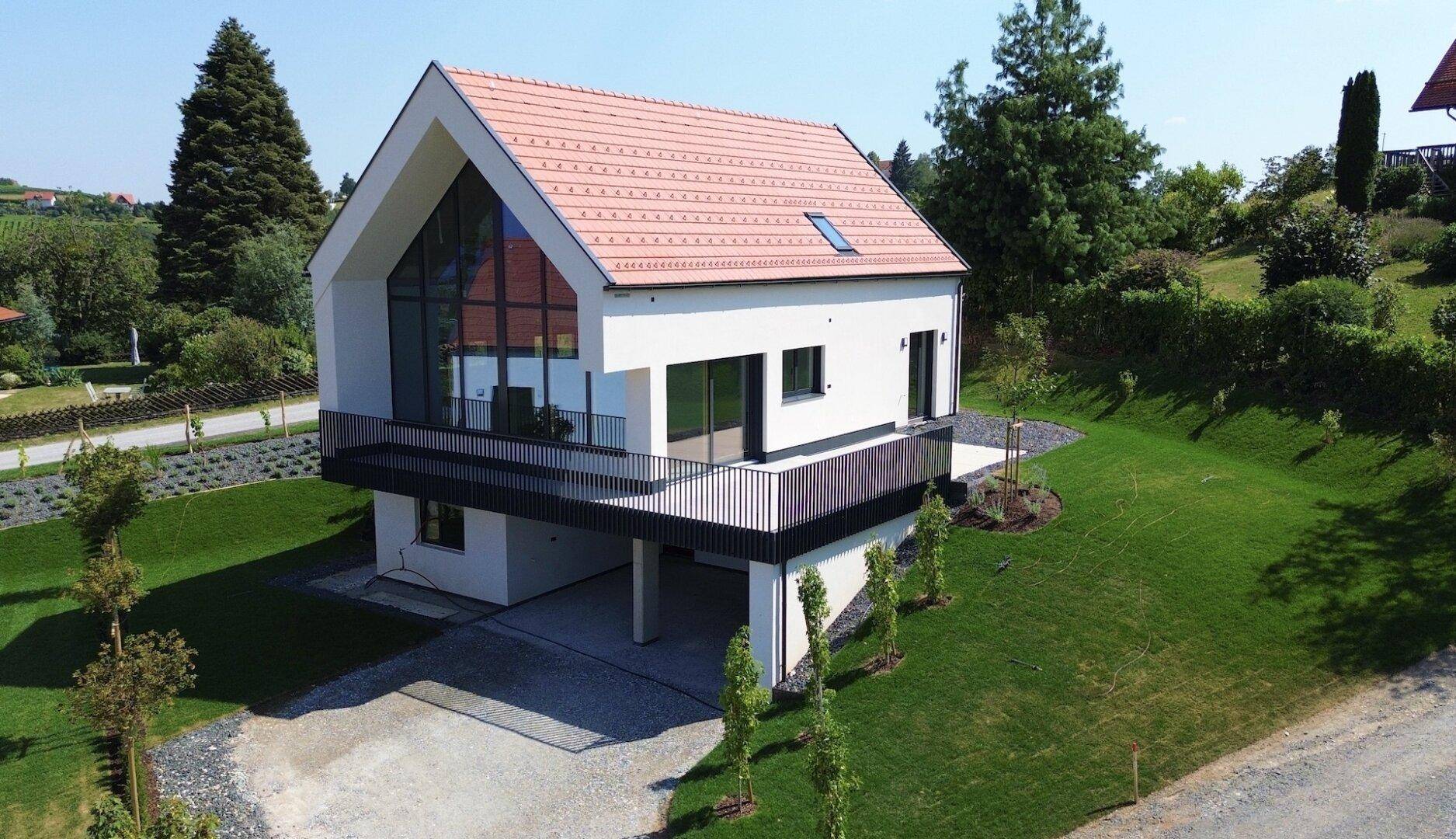 Freistehendes modernes Haus mit Balkon und großer Glasfront, umgeben von gepflegtem Rasen und Bäumen.