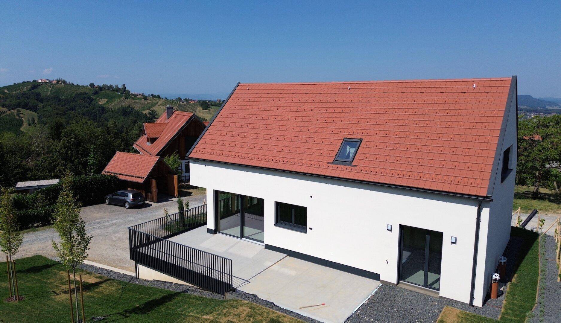 Rückseite eines modernen Hauses mit großer Terrasse und Blick auf die umliegende Hügellandschaft.