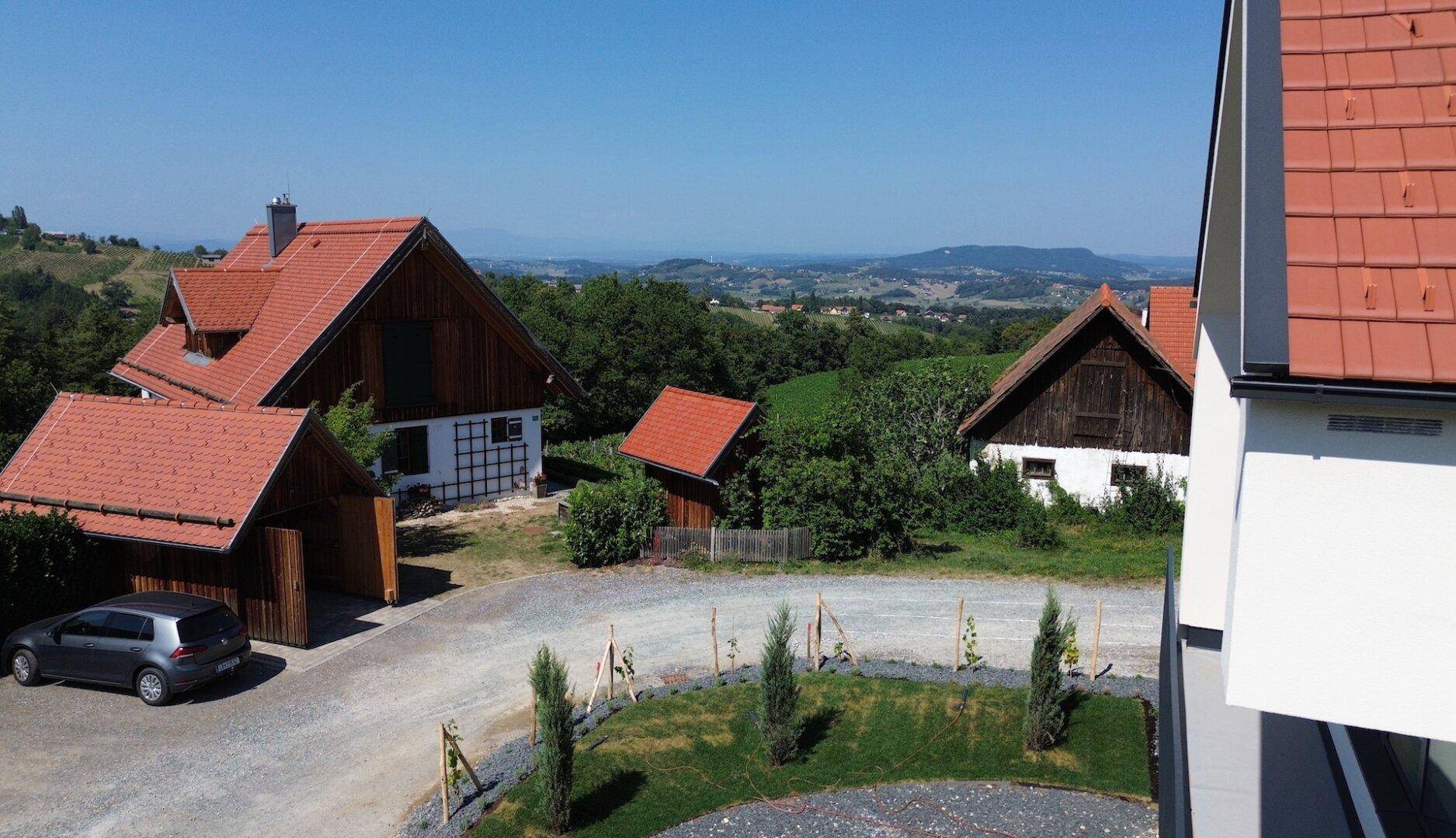 Weitläufiger Blick über die ländliche Umgebung mit traditionellen Häusern und grünen Hügeln unter blauem Himmel.