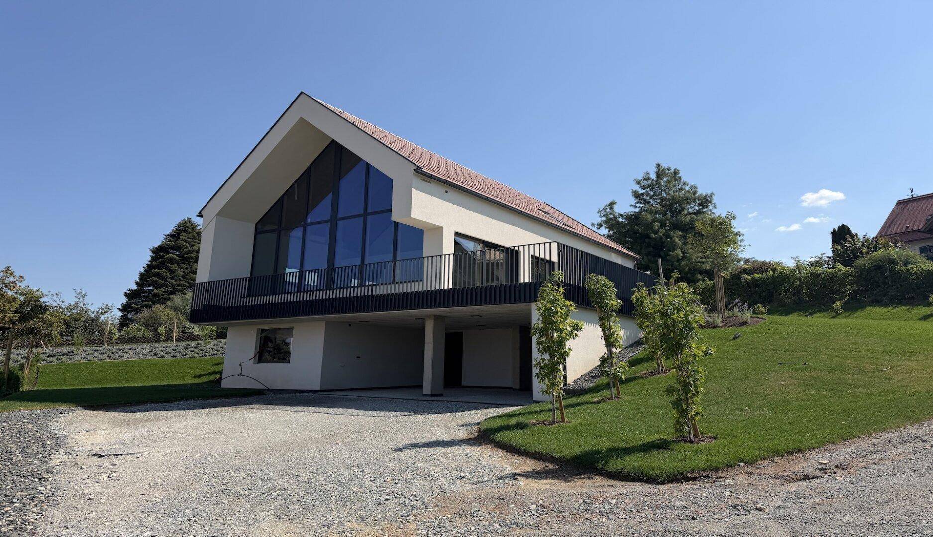 Modernes Einfamilienhaus mit beeindruckender Glasfassade, Balkon und überdachtem Stellplatz im Erdgeschoss.