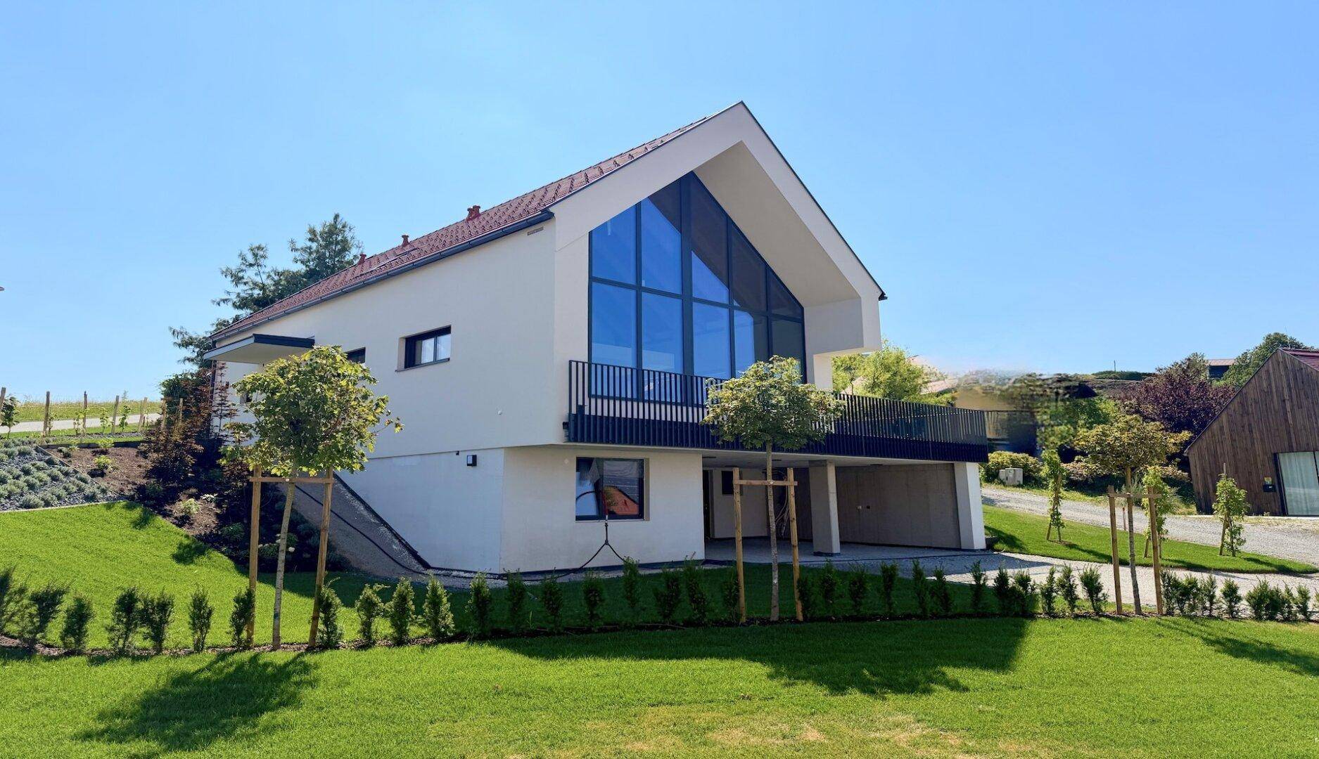 Modernes Haus mit markanter Glasfassade und gepflegtem Vorgarten mit Hecken und jungen Bäumen.