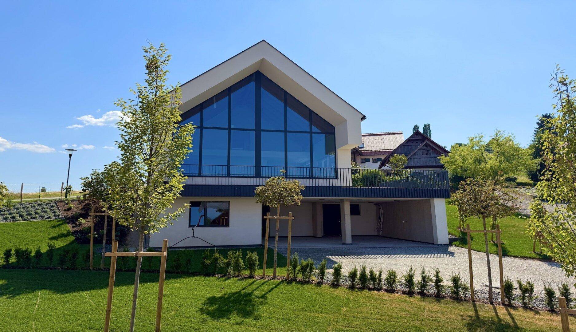 Elegantes modernes Haus mit großer Glasfront und einladendem Eingangsbereich, umgeben von Grünflächen.