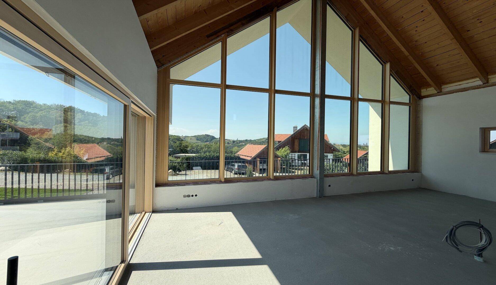 Großzügiger, heller Wohnraum im Rohbau mit hoher Holzdecke und beeindruckender Glasfront mit Weitblick.