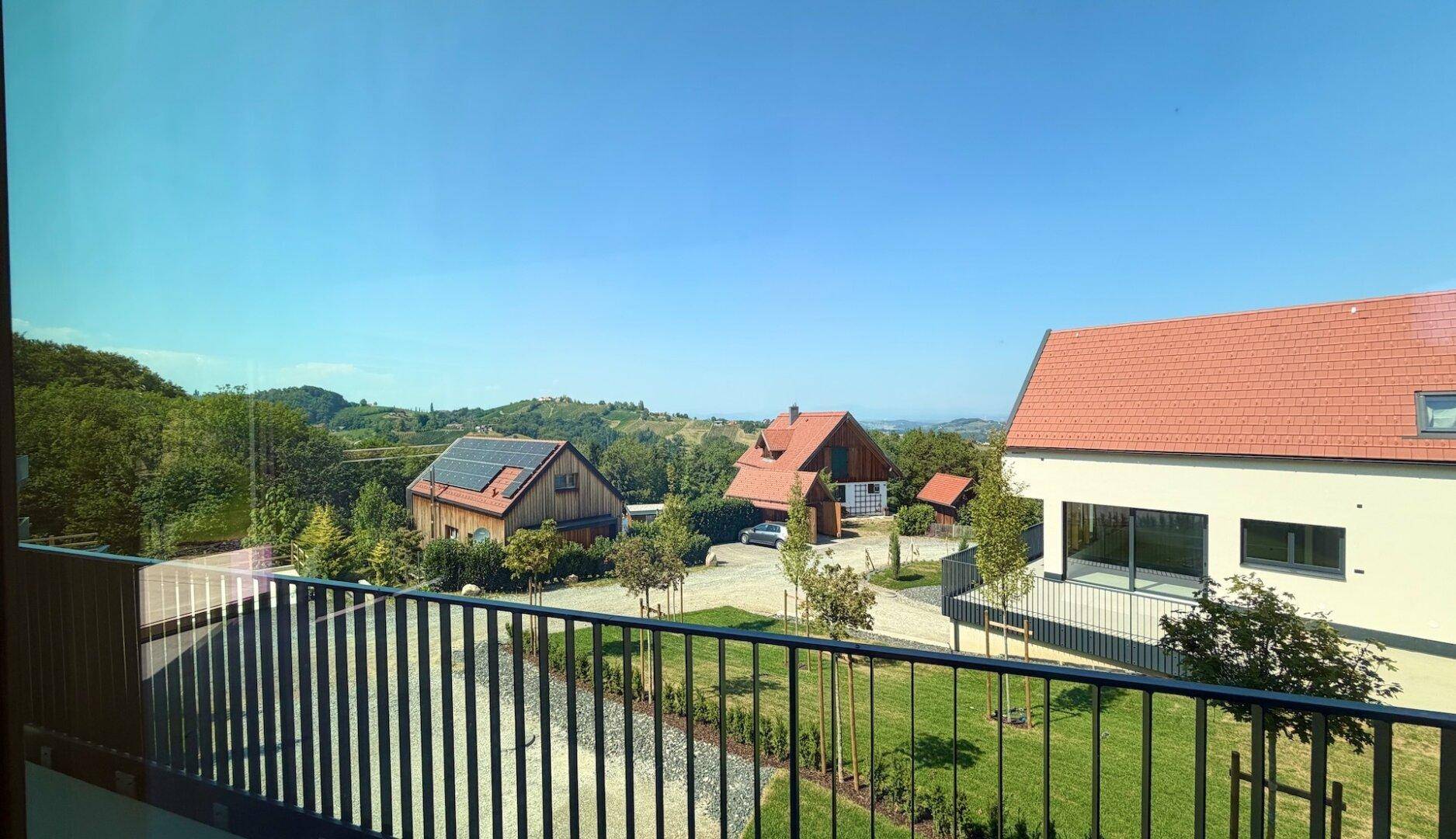 Panoramablick aus dem Innenraum durch die Glasfassade auf den Balkon, Rasen und die weite Landschaft.