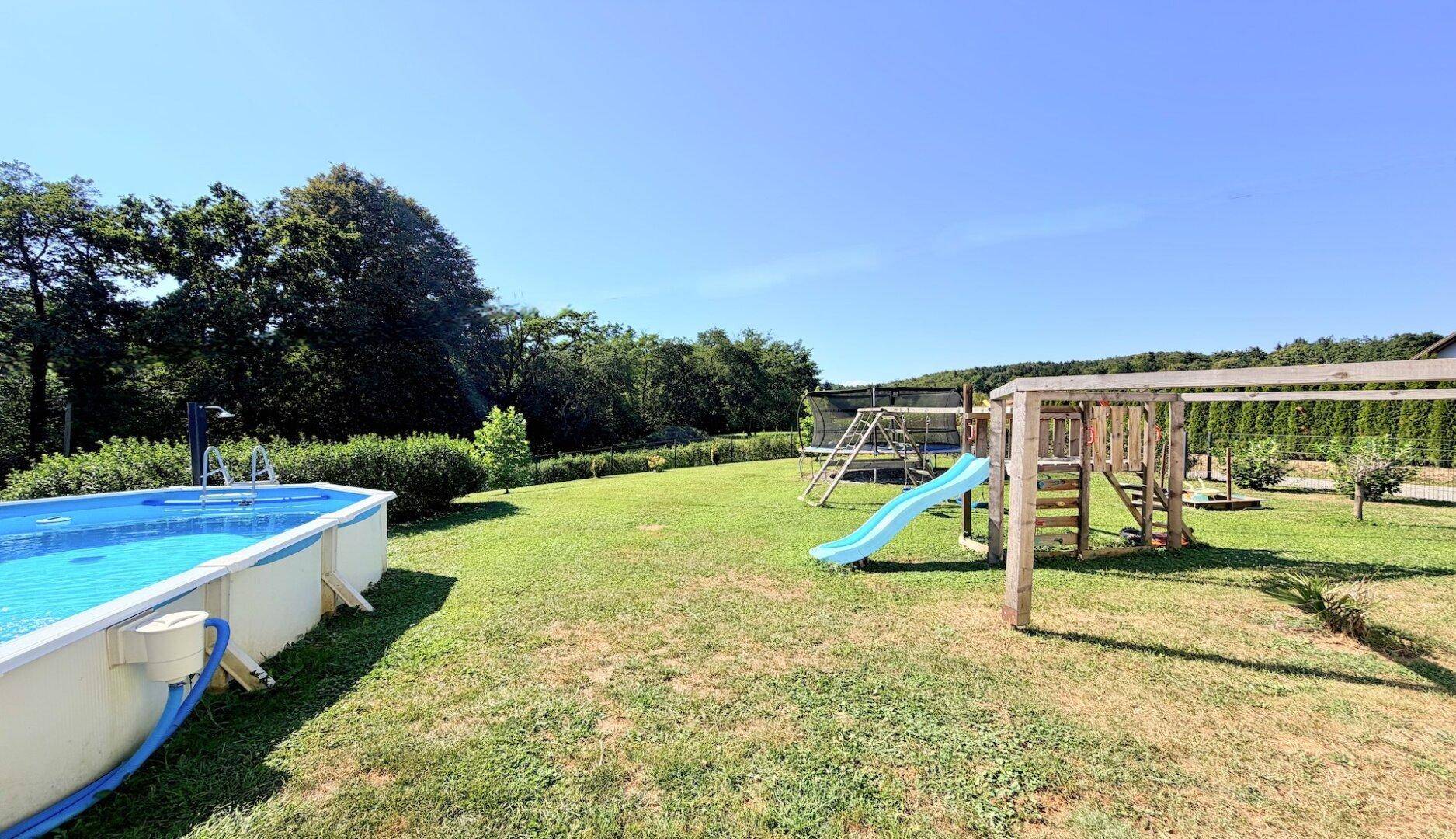 Großer Gartenbereich mit Aufstellpool und Holzspielplatz unter blauem Himmel.