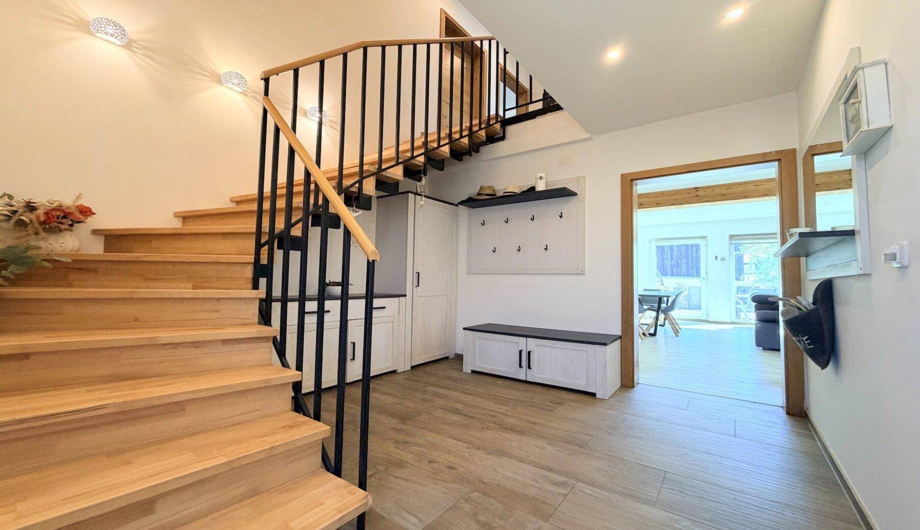 Heller Eingangsbereich mit Holztreppe, Garderobe und modernem Fliesenboden.