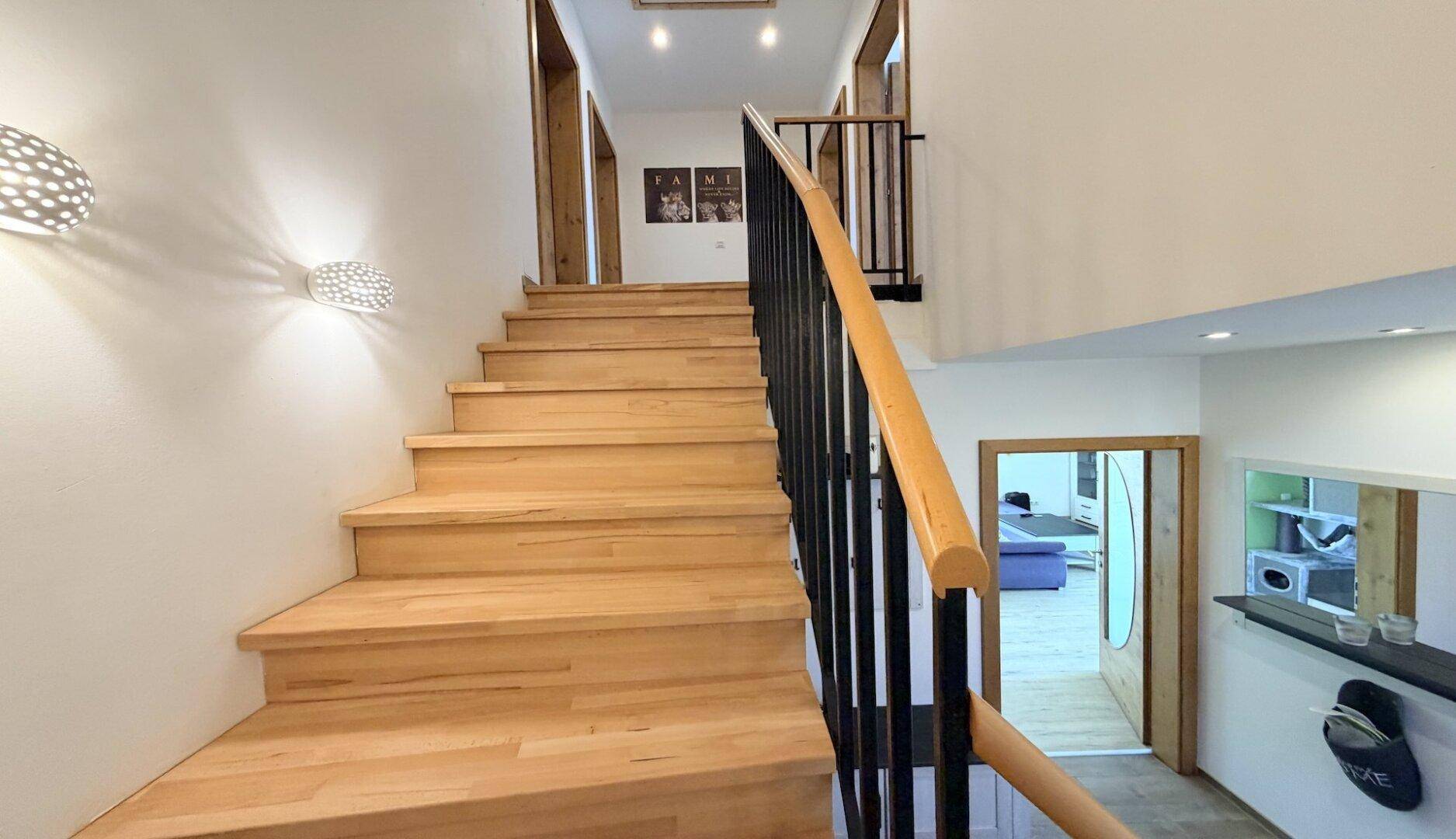 Holztreppe mit schwarzem Geländer führt in das obere Stockwerk des Hauses.