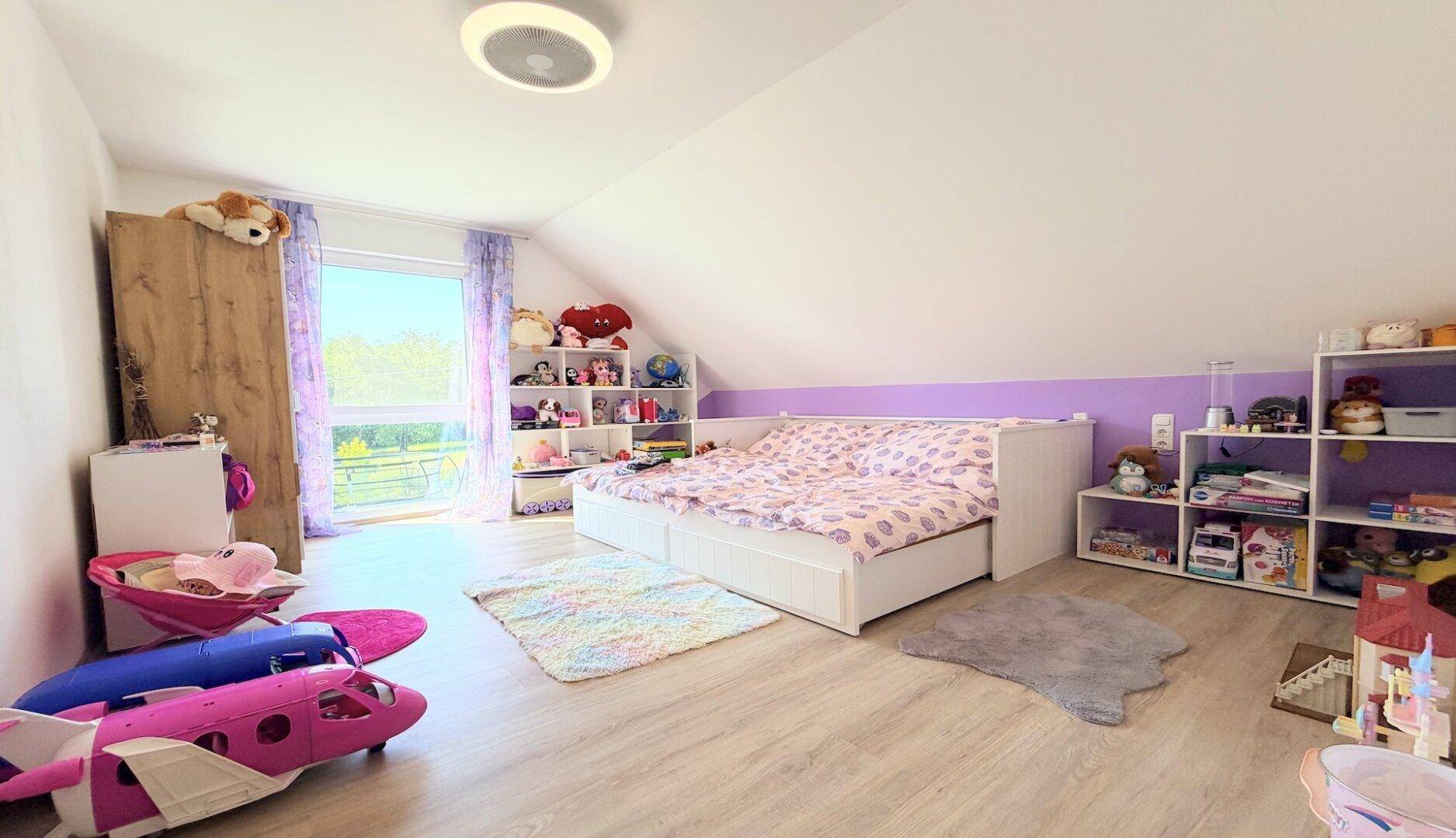 Kinderzimmer im Dachgeschoss mit schrägen Wänden, Laminatboden und großem Fenster.