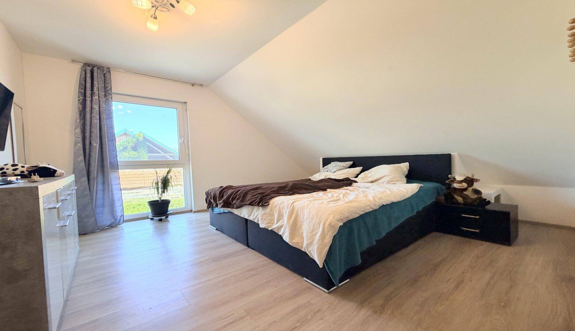 Schlafzimmer im Dachgeschoss mit Doppelbett, Laminatboden und großem Fenster.