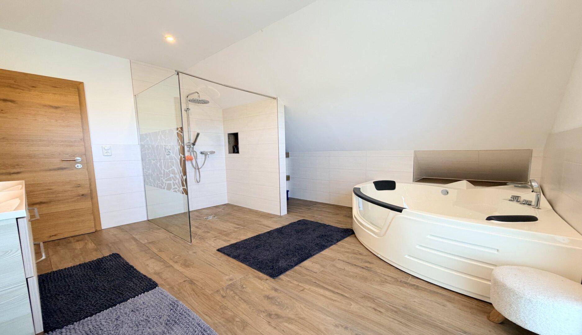 Geräumiges Badezimmer mit Eckbadewanne und großer Glasdusche im Dachgeschoss.