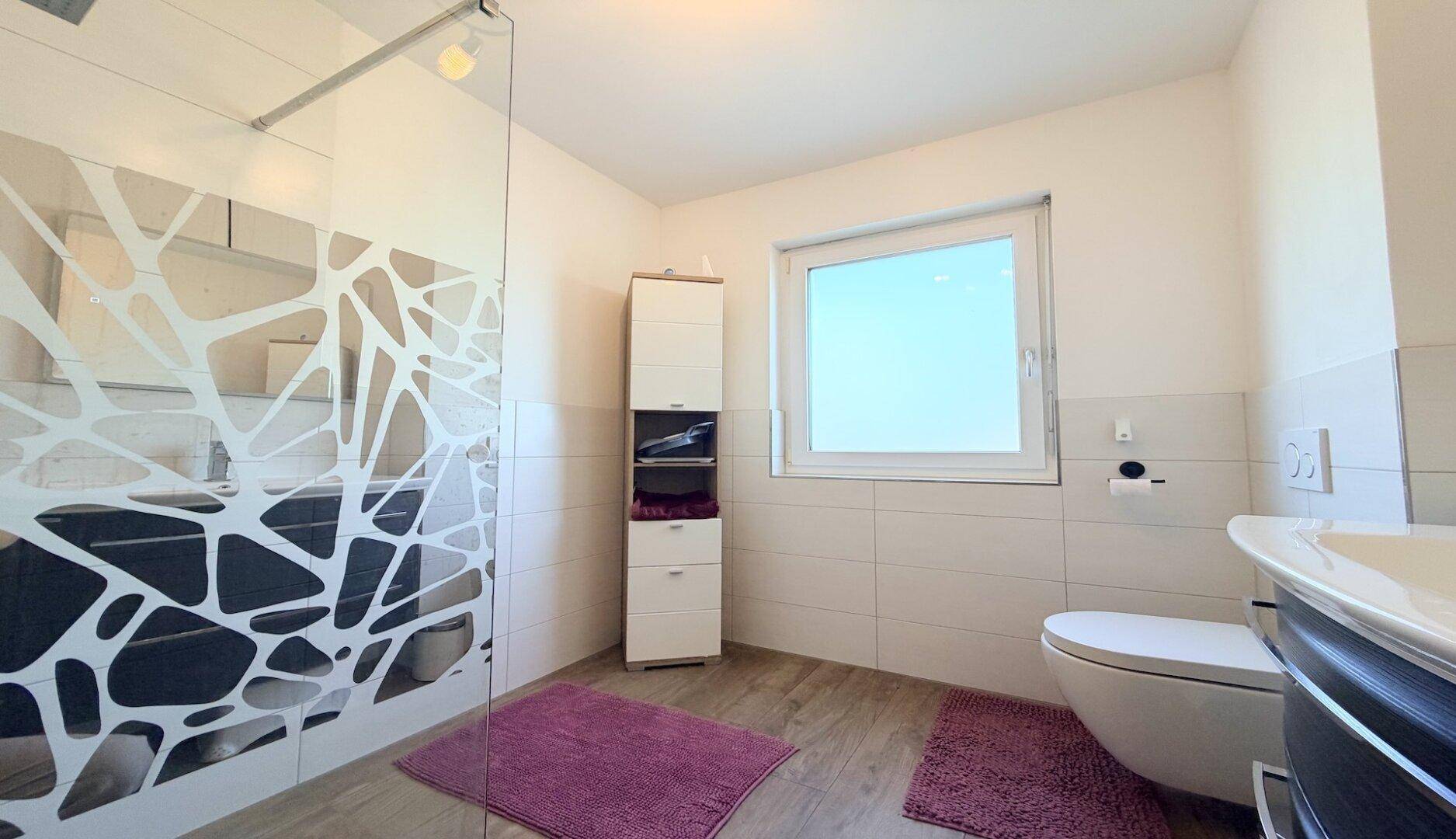 Helles Badezimmer mit Dusche, WC und Fenster im Dachgeschoss.