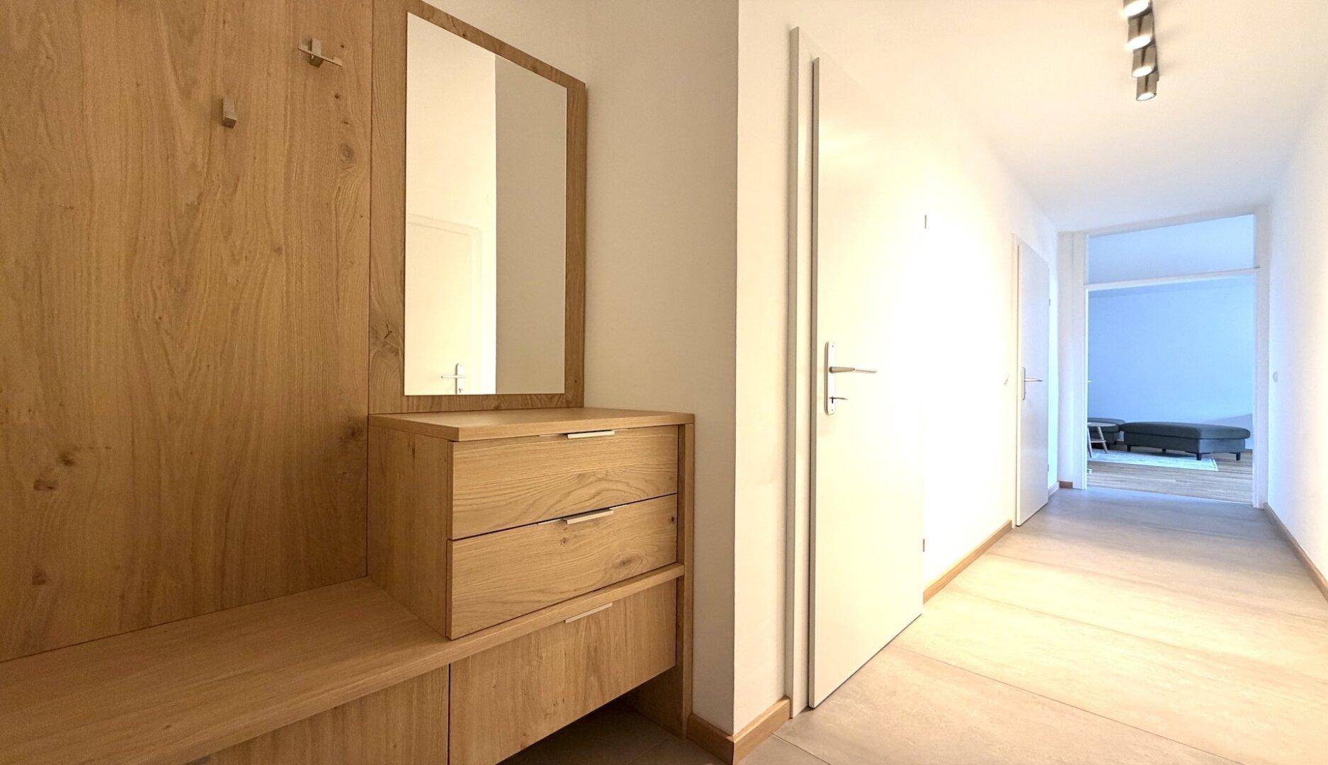 Heller Eingangsbereich mit moderner Holzgarderobe und Spiegel, führt zu weiteren Räumen.