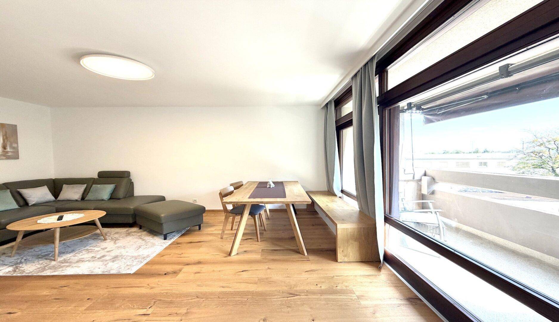 Heller Wohn- und Essbereich mit Holzboden, gemütlichem Sofa und Zugang zum Balkon.