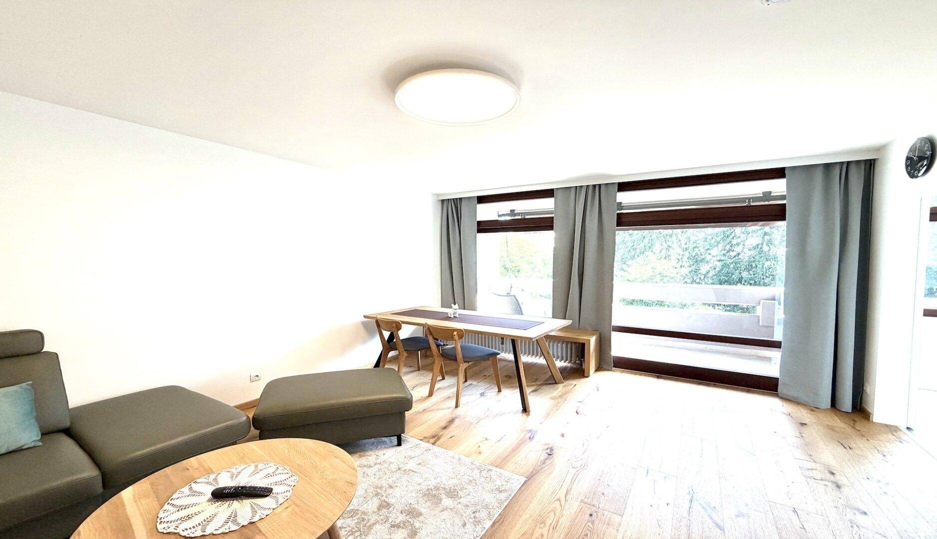 Lichtdurchfluteter Wohn- und Essbereich mit Holzboden und großen Fenstern zum Balkon.