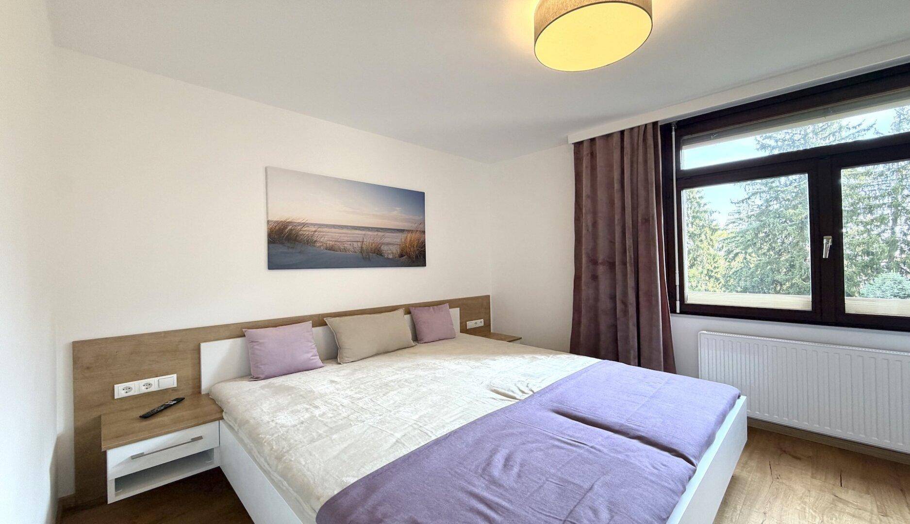 Helles Schlafzimmer mit Doppelbett, Nachttischen und Fenster mit Blick ins Grüne.