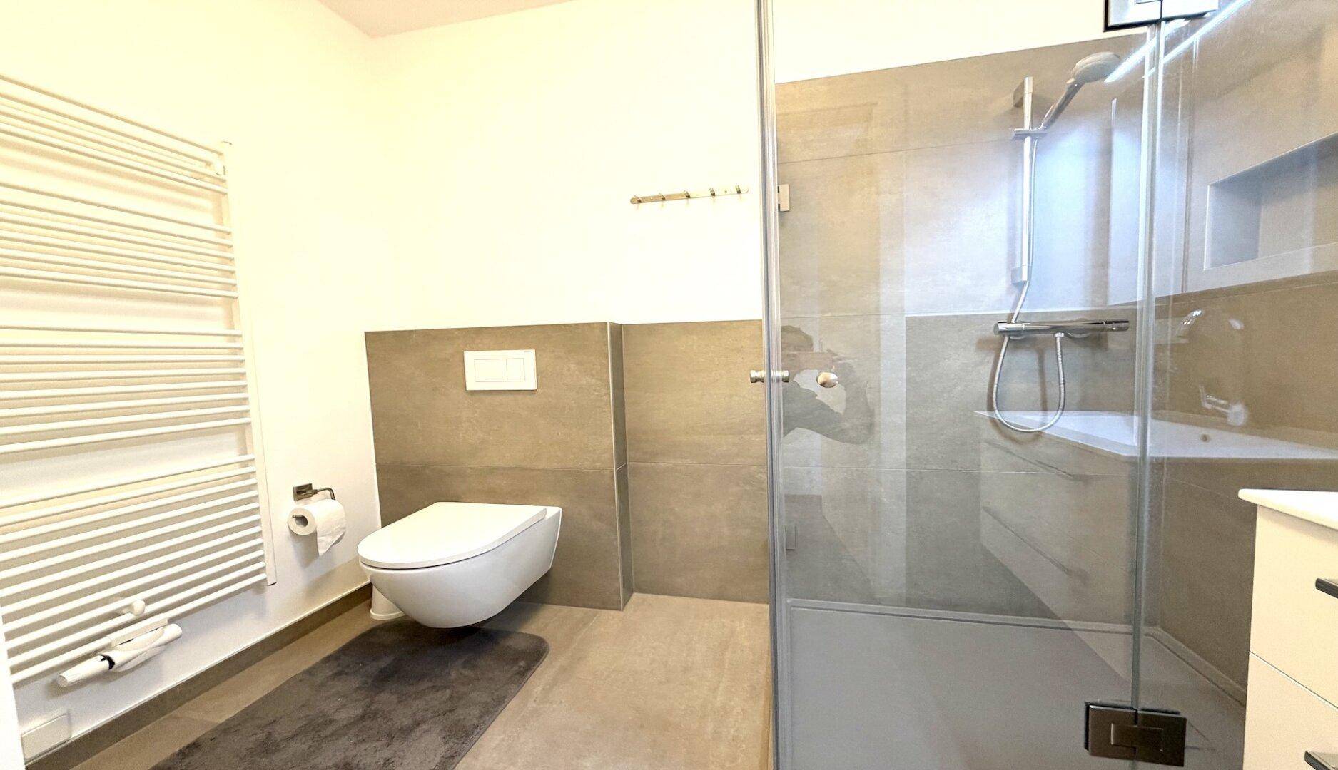 Helles Badezimmer mit großer Glasdusche, Wand-WC und beheiztem Handtuchhalter.