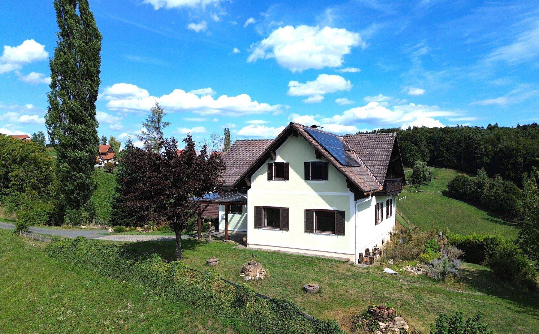 Einfamilienhaus mit Photovoltaikanlage auf dem Dach, umgeben von grünen Wiesen und Bäumen.
