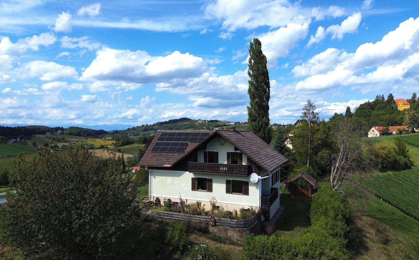 Wohnhaus mit Photovoltaikanlage und Balkon, eingebettet in eine grüne Hügellandschaft.