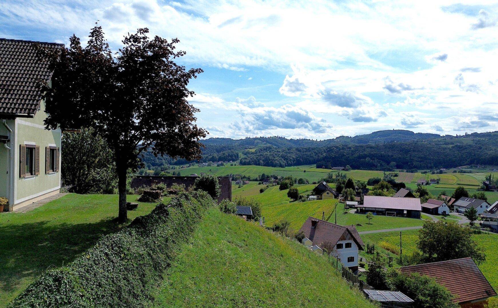 Teilansicht eines Hauses mit Blick auf eine ausgedehnte, grüne Landschaft und ein Dorf.