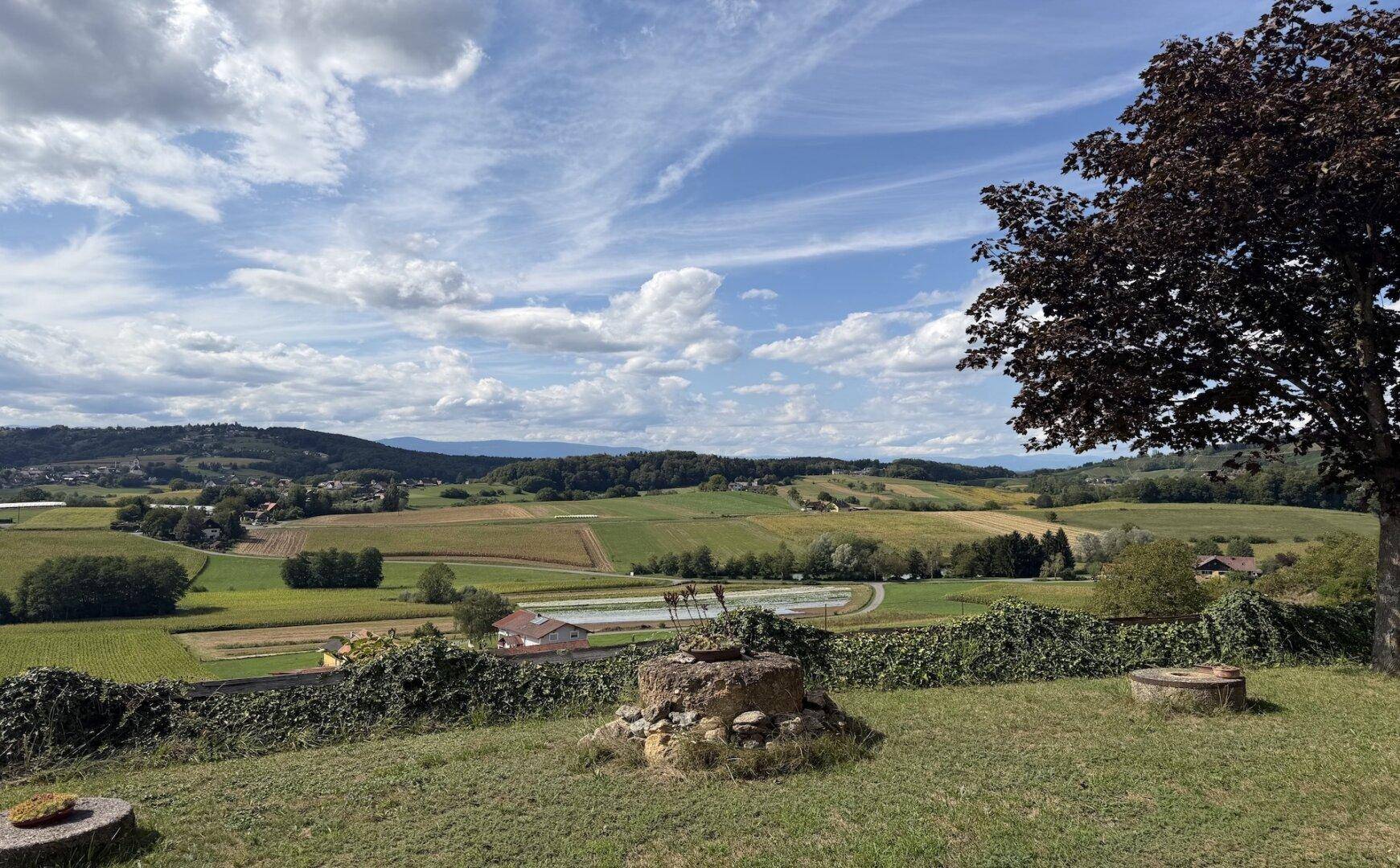 Gepflegter Gartenbereich mit Blick auf die weite, grüne Hügellandschaft unter blauem Himmel.