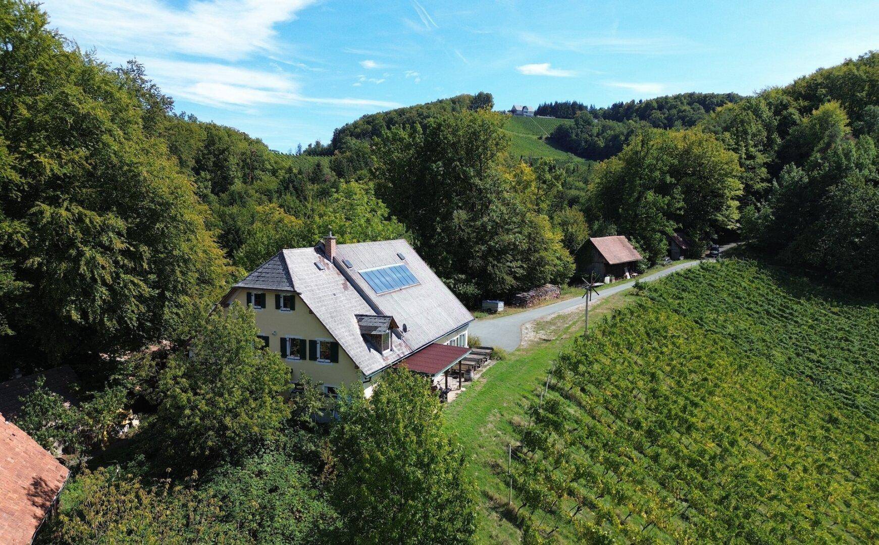 Haus mit Solaranlage auf dem Dach, eingebettet in grüne Hügellandschaft und Wald.
