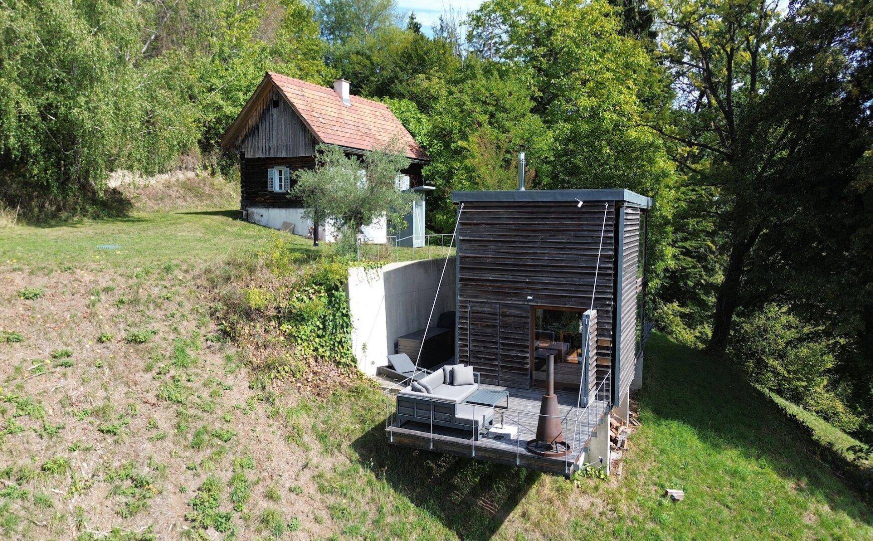 Drohnenaufnahme von zwei Häusern in einer idyllischen, bewaldeten Hügellandschaft mit Terrasse.