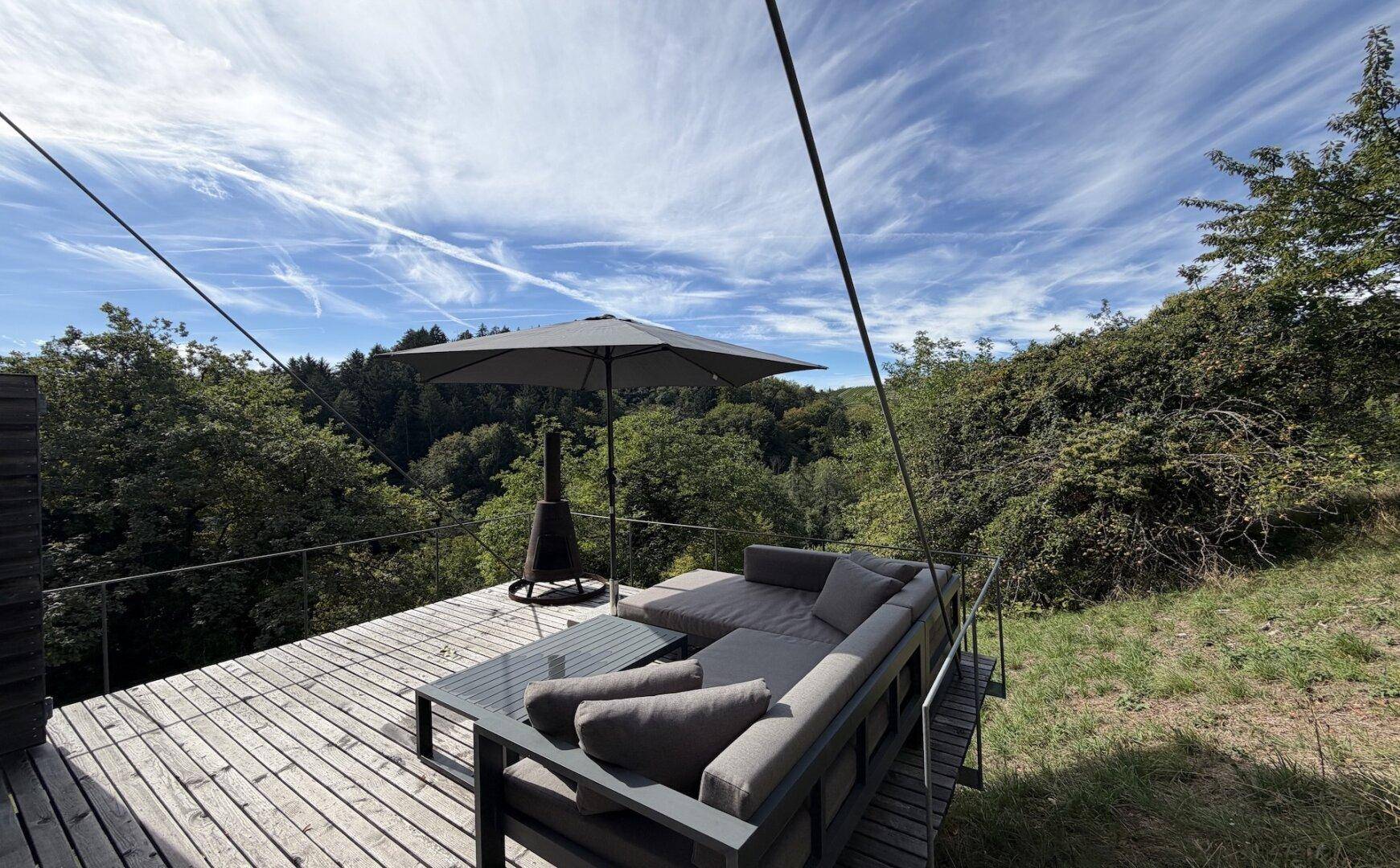 Weitläufige Holzterrasse mit Lounge-Möbeln und weitem Blick über die bewaldete Hügellandschaft.