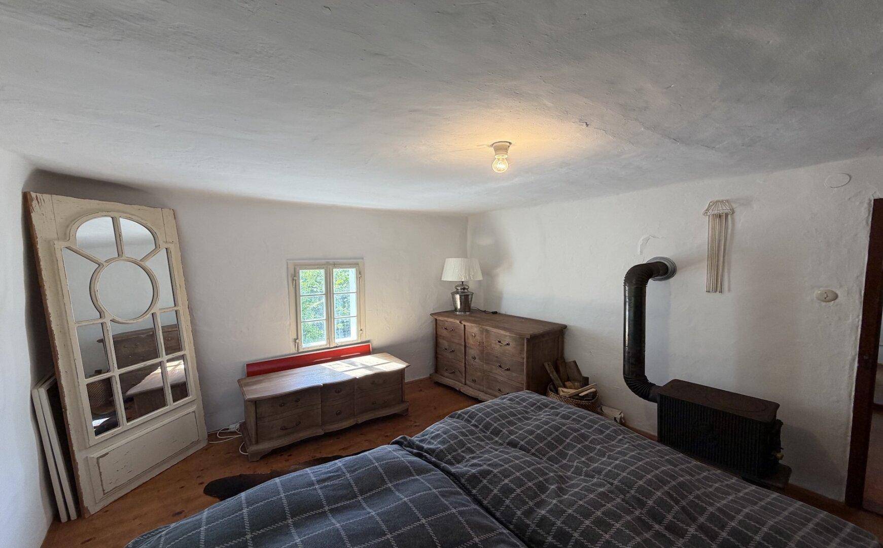 Gemütliches Schlafzimmer im traditionellen Stil mit Holzboden, Ofen und Blick ins Grüne.